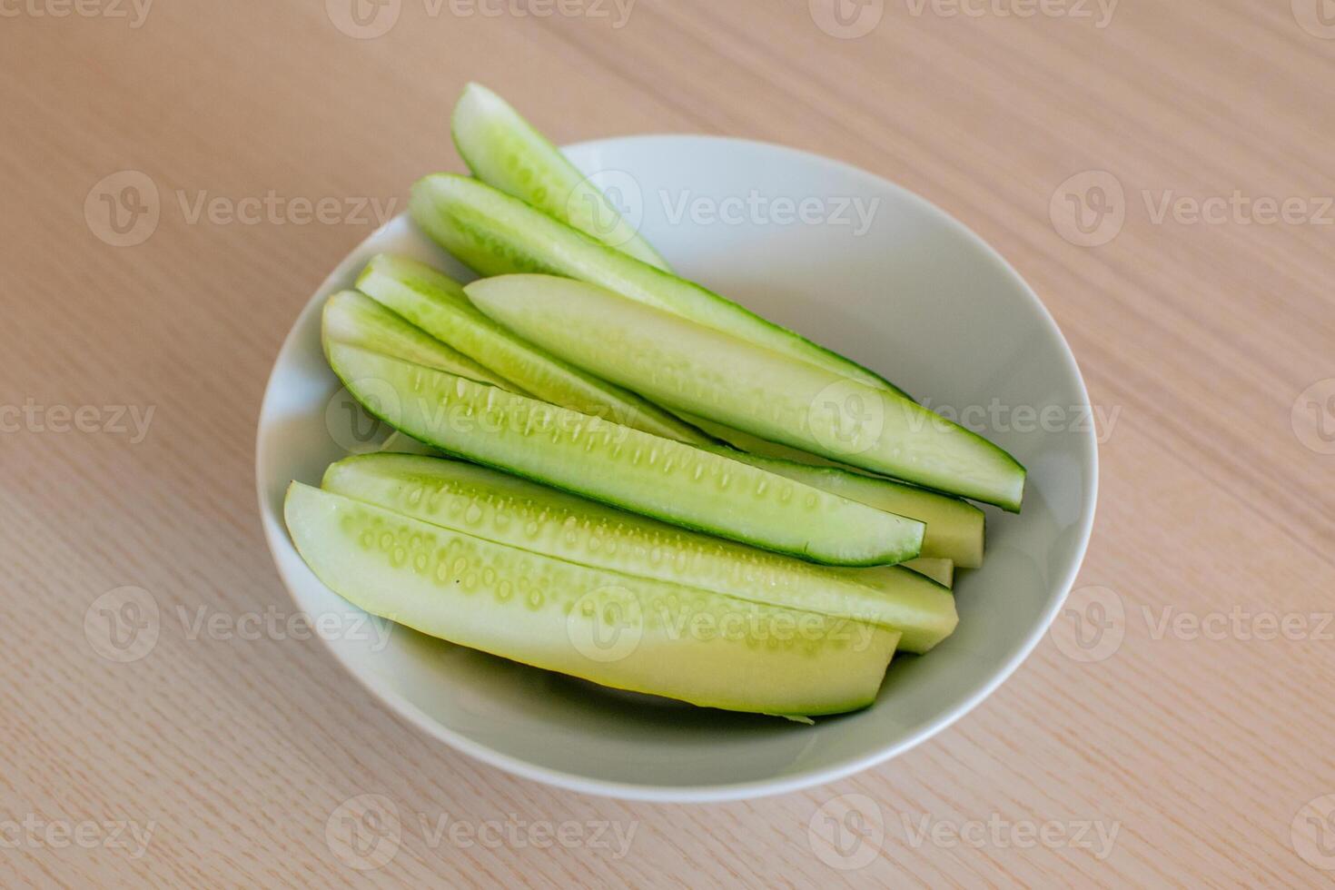 Freshly sliced cucumbers in a white bowl on a wooden table, ideal for healthy eating and summer salad recipes photo