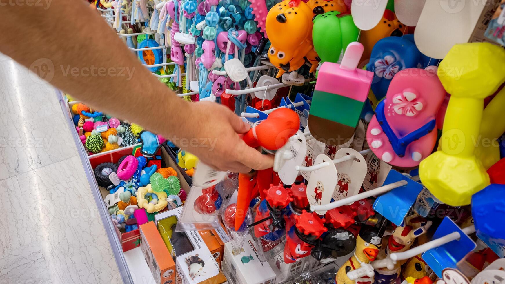A persons hand selecting colorful dog toys from a diverse display in a pet store, highlighting pet care and choices photo