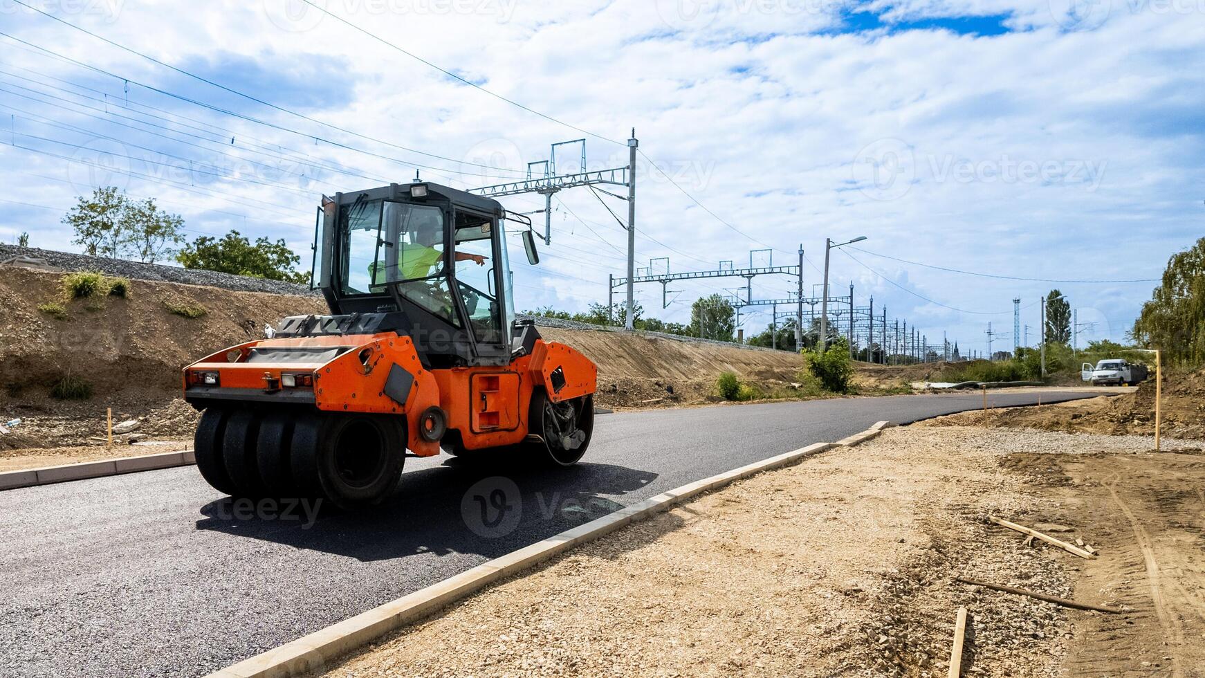 An orange steamroller compacts freshly paved asphalt on a rural road, enhancing infrastructure development and road safety photo