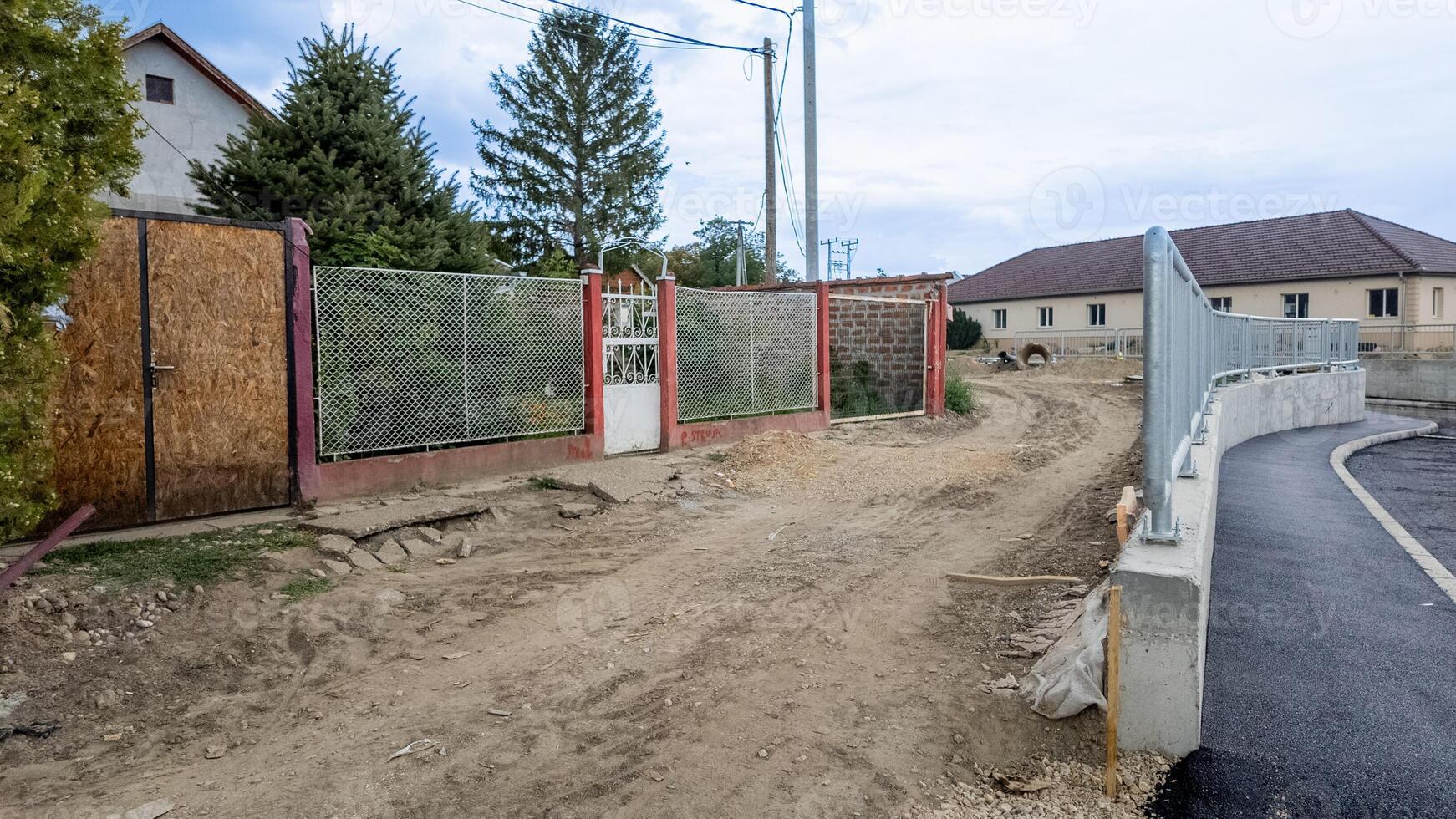 Rural dirt road leading to residential houses, illustrating infrastructure challenges and urban development in small European village settings photo