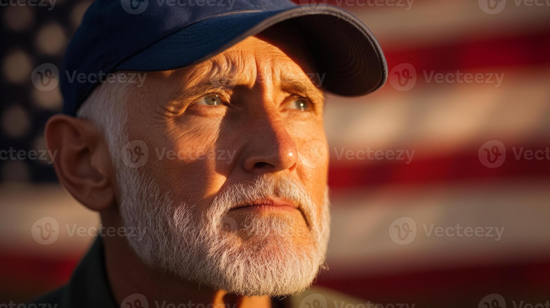 Elderly US veteran at sunrise with a shadowy American flag waving behind wearing a navy blue cap strong gaze warm golden light reflecting off face background with space for text photo