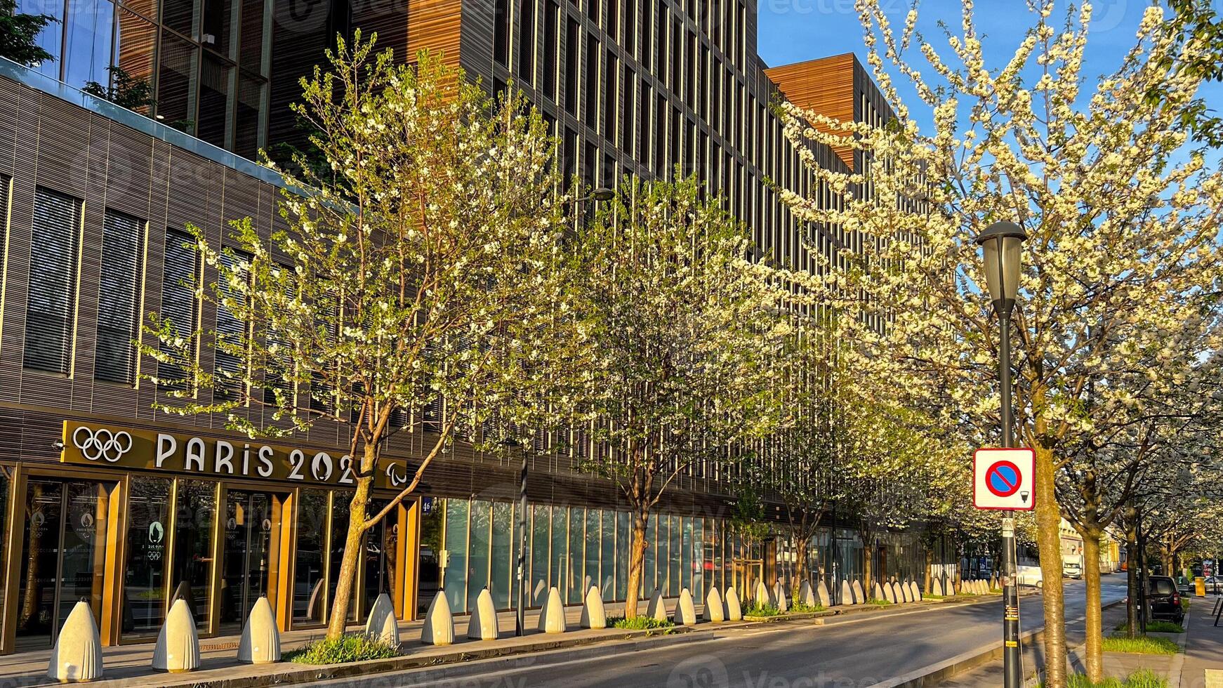 Blooming trees line a street next to a building with Paris 2024 signage, symbolizing preparation for the Olympics photo
