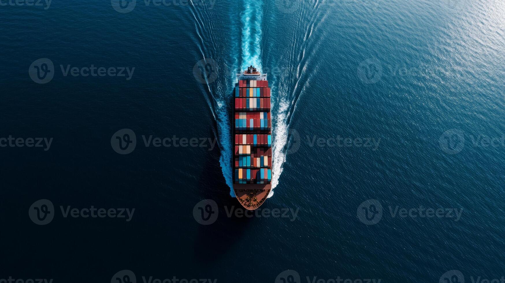 Aerial shot of a cargo ship filled with multi colored containers cruising through calm ocean waters sunlight reflecting off the surface as it creates a wide wake photo