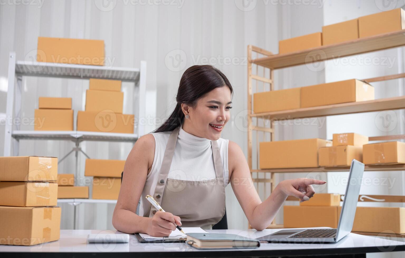 Woman Packing Boxes of Merchandise for Online Sale in a Modern Workspace with Shelves and Laptop photo