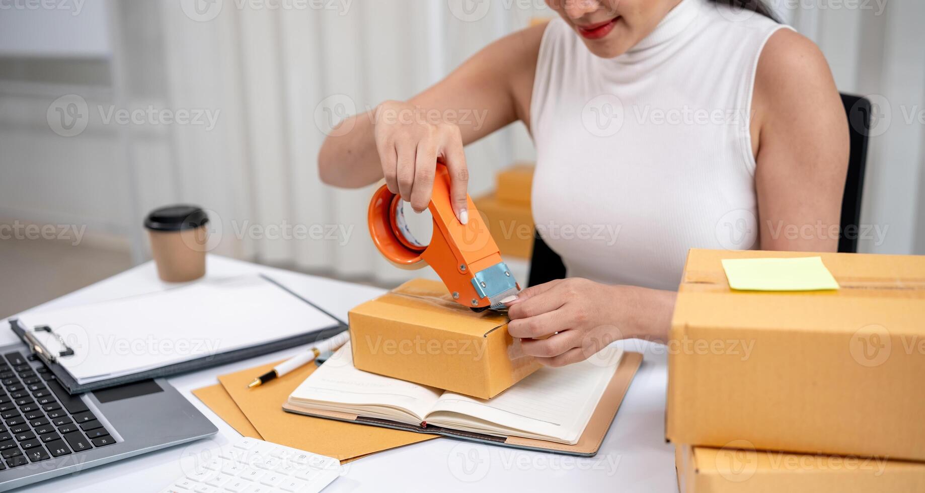 Woman Packing Boxes of Merchandise for Online Sales in a Modern Home Office Setting with Laptop and Coffee photo
