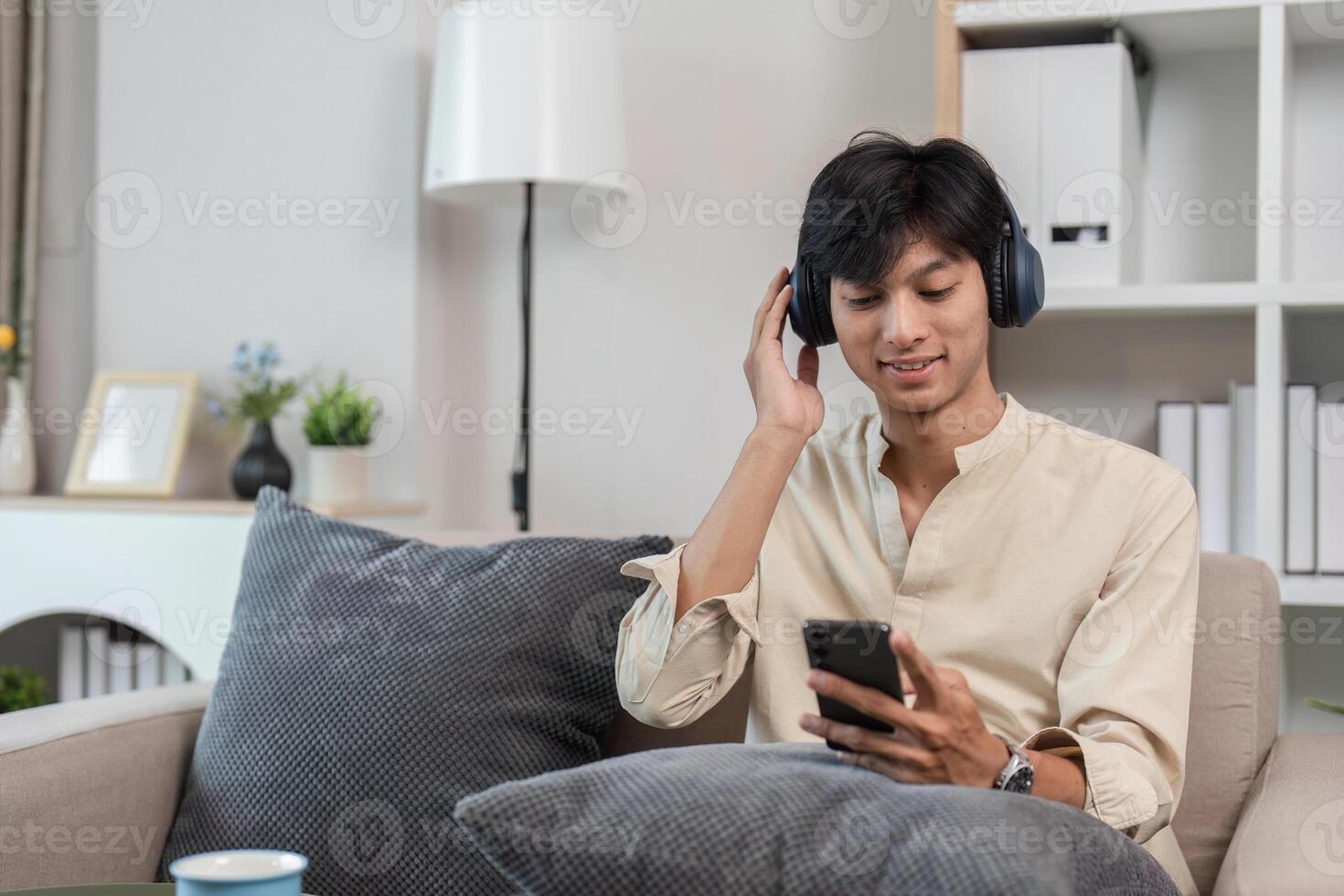 Young Man Relaxing in Modern Room While Playing on Phone and Listening to Music with Headphones photo