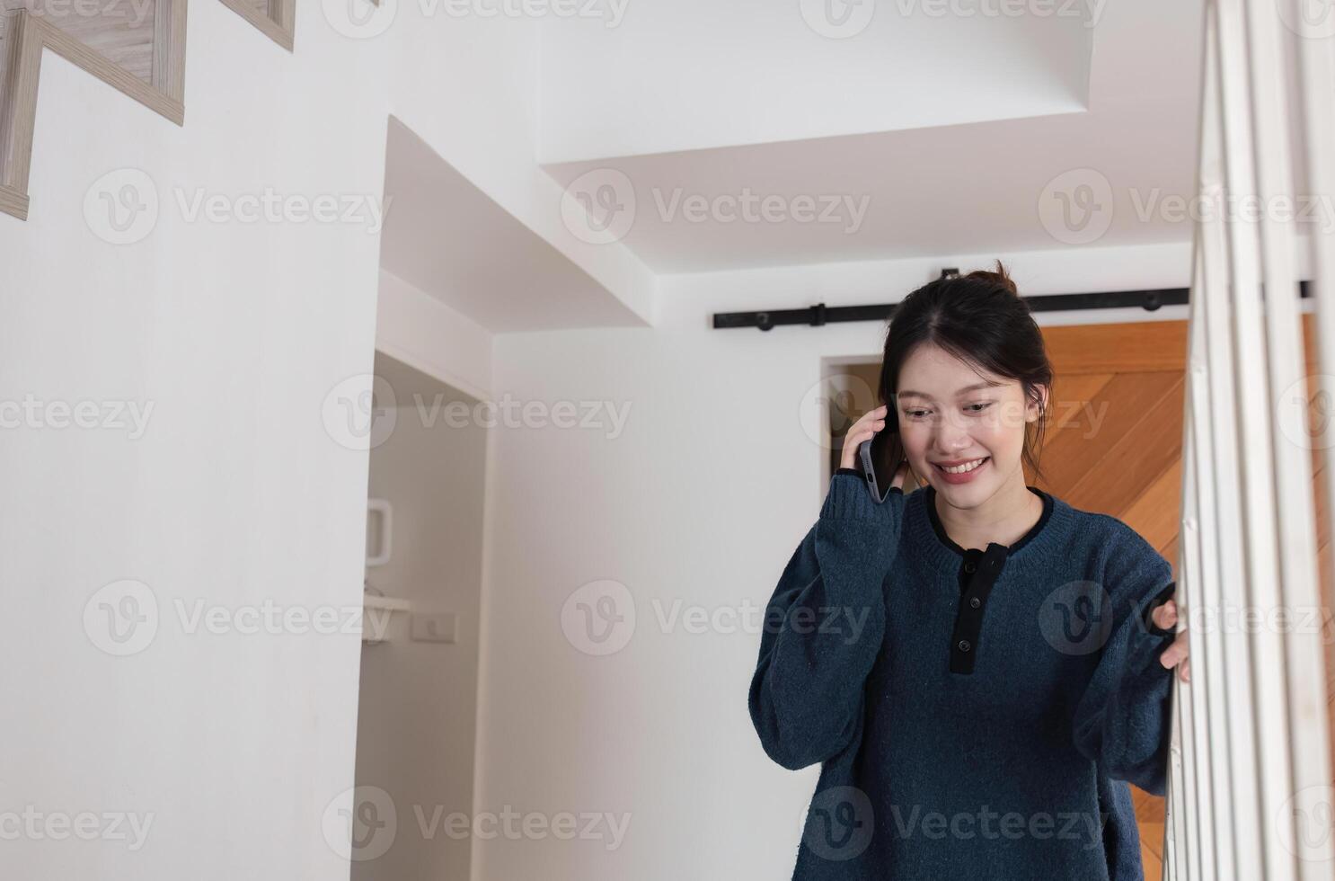 Young Woman Smiling While Talking on the Phone in a Modern Home Interior with Wooden Door Background photo