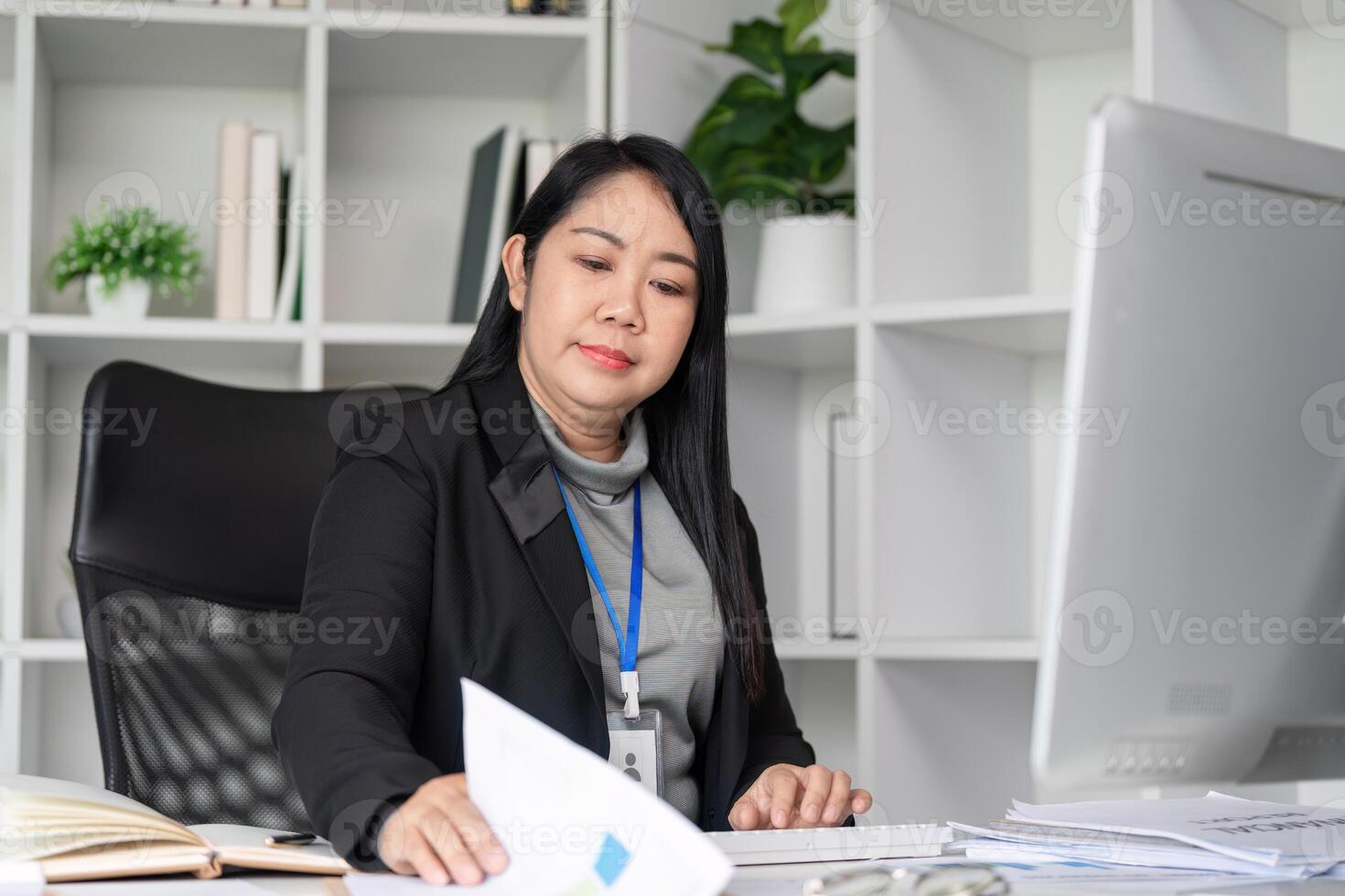 Middle-Aged Business Woman Working at Desk in Modern Office Environment with Documents and Computer photo