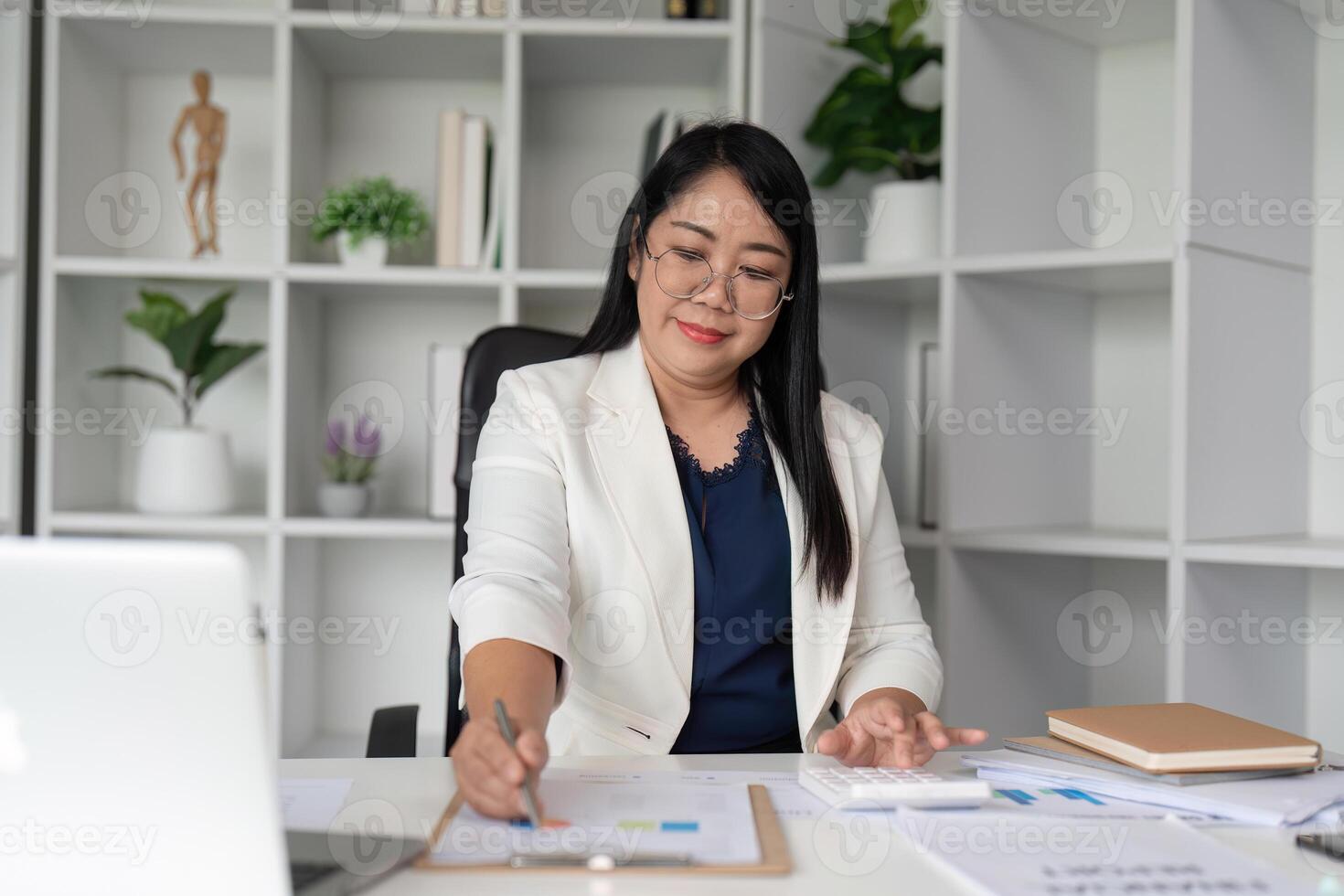 Middle Aged Business Woman Working at Desk in Modern Office with Documents and Laptop photo