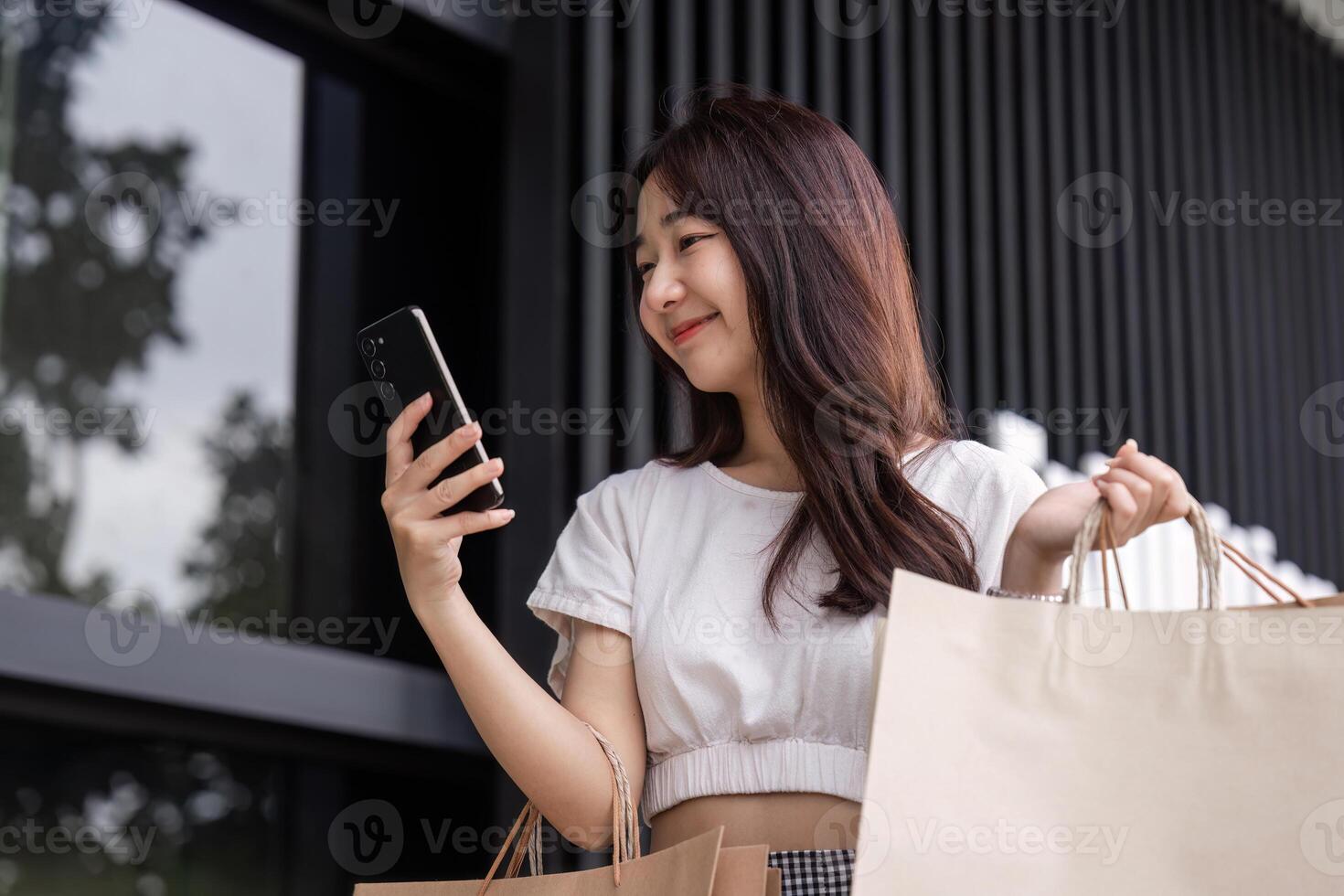 Smiling Woman Holding Shopping Bags at the Mall While Checking Her Smartphone for the Latest Deals and Offers photo