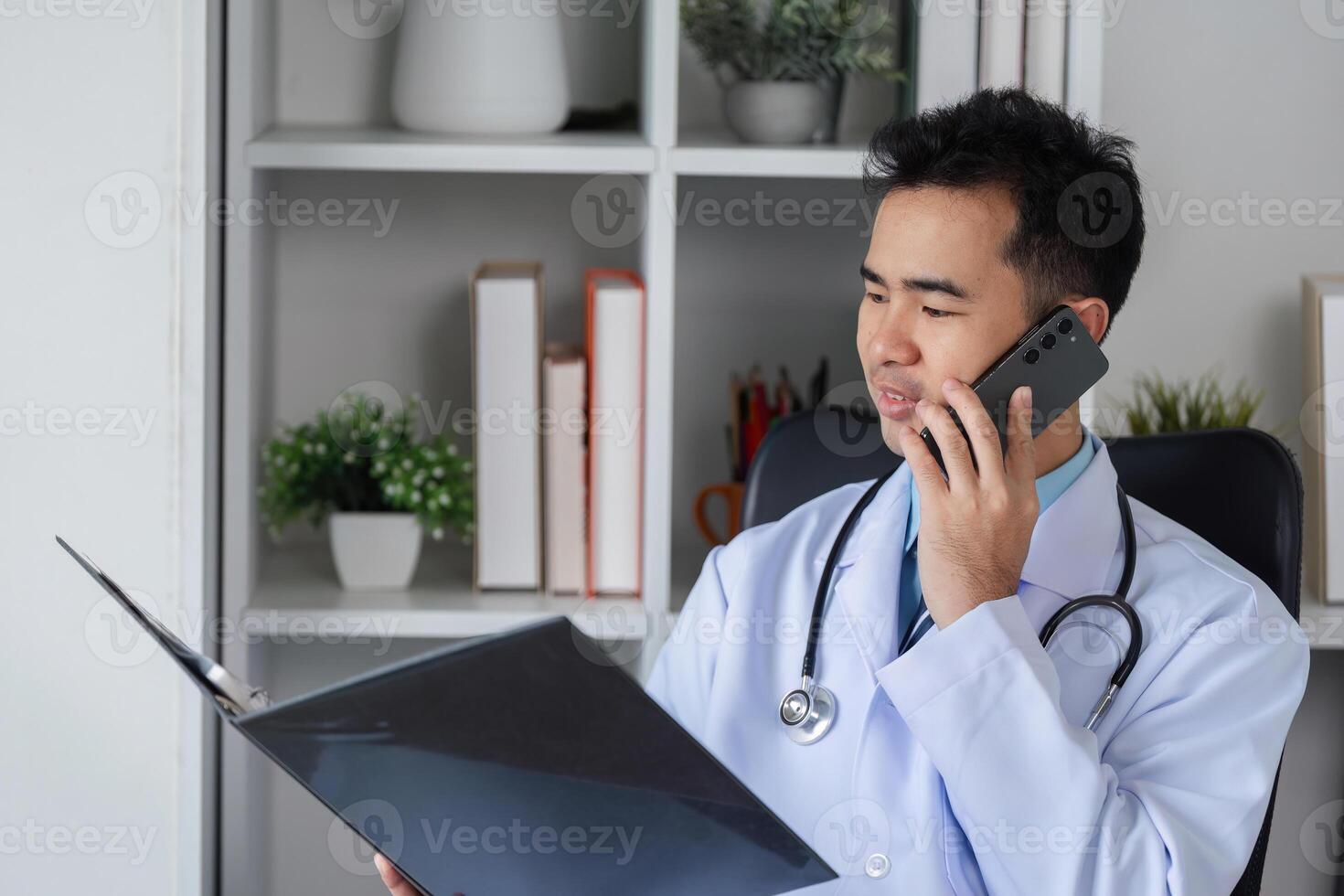 Confident Male Doctor in White Coat Discussing Patient Care on Phone in Modern Medical Office Setting photo