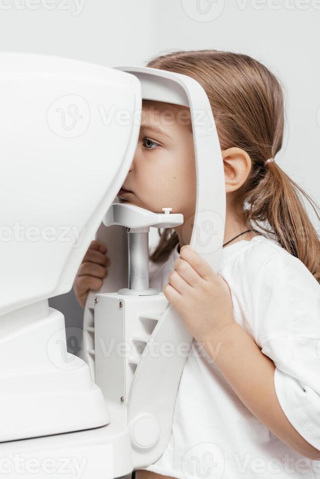Portrait of a little, happy girl in ophthalmology clinic. Ophthalmic instrument. Excellent moment to illustrate careful examination for children's eye health. Advertisement for pediatric ophthalmology photo