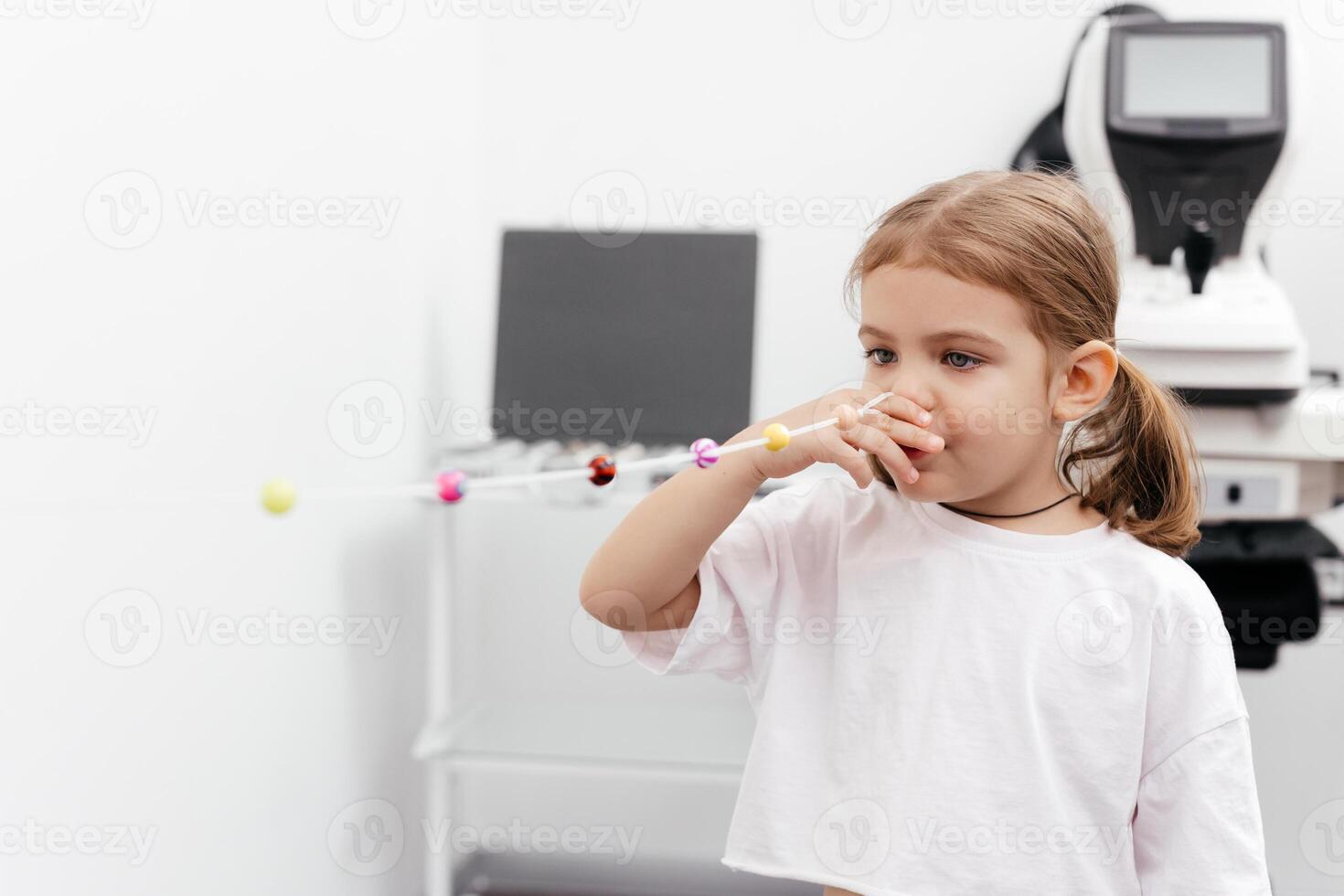 Portrait of a little, happy girl in ophthalmology clinic. Ophthalmic instrument. Excellent moment to illustrate careful examination for children's eye health. Advertisement for pediatric ophthalmology photo