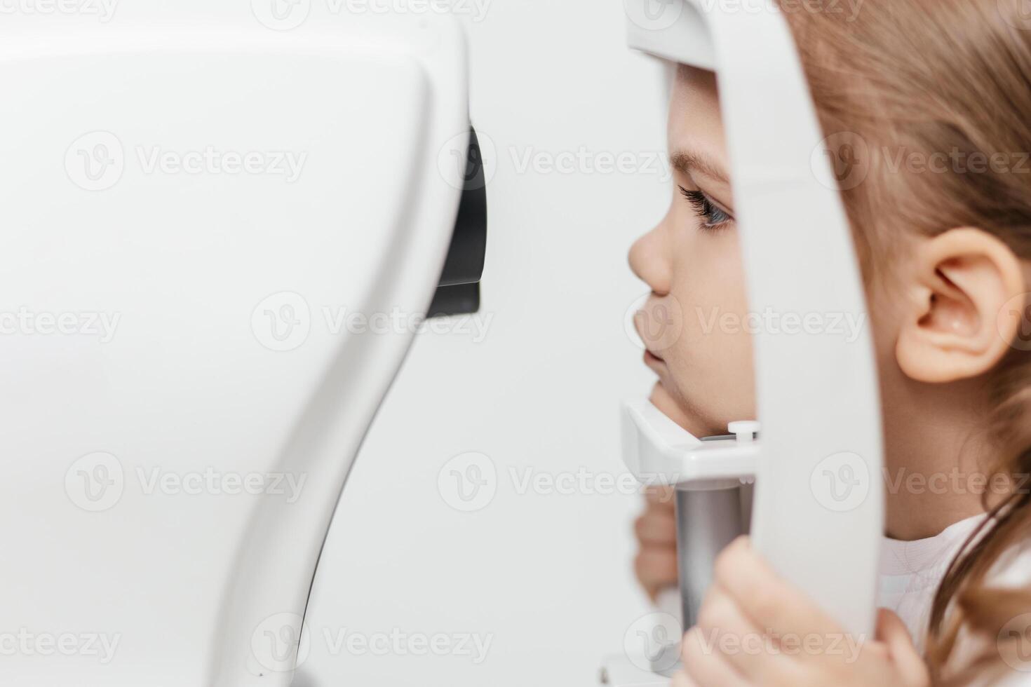 Portrait of a little, happy girl in ophthalmology clinic. Ophthalmic instrument. Excellent moment to illustrate careful examination for children's eye health. Advertisement for pediatric ophthalmology photo