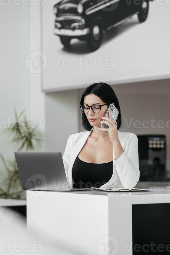 Professional sales manager talking, consulting about auto to female client in dealership by smartphone and helps to choose electric car. Buying, renting and insuring a car. photo