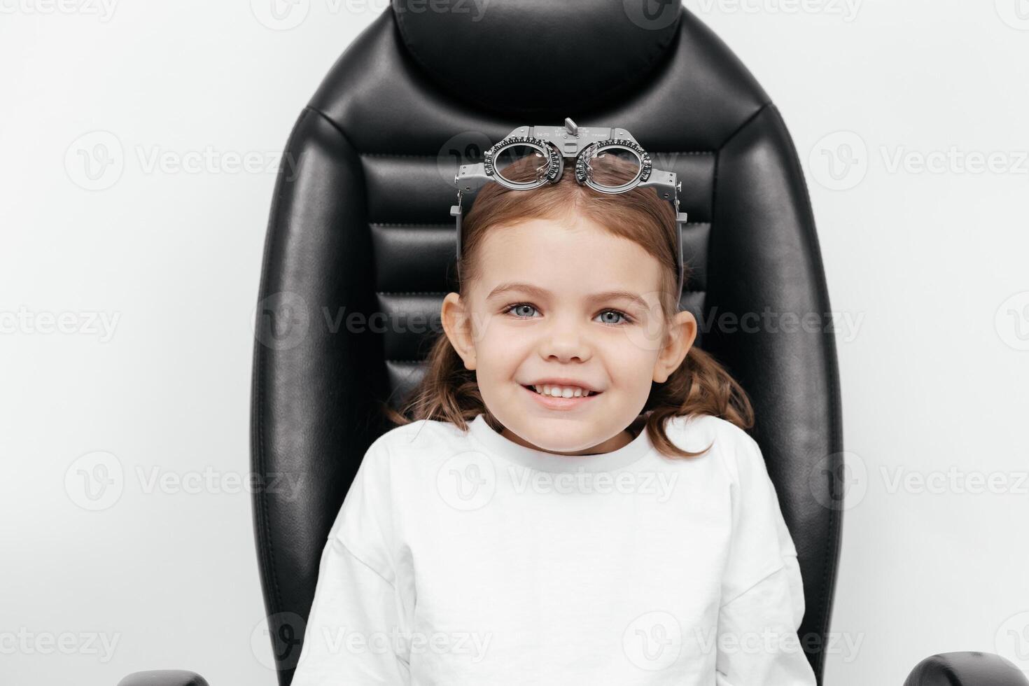 Portrait of a little, happy girl in ophthalmology clinic. Ophthalmic instrument. Excellent moment to illustrate careful examination for children's eye health. Advertisement for pediatric ophthalmology photo