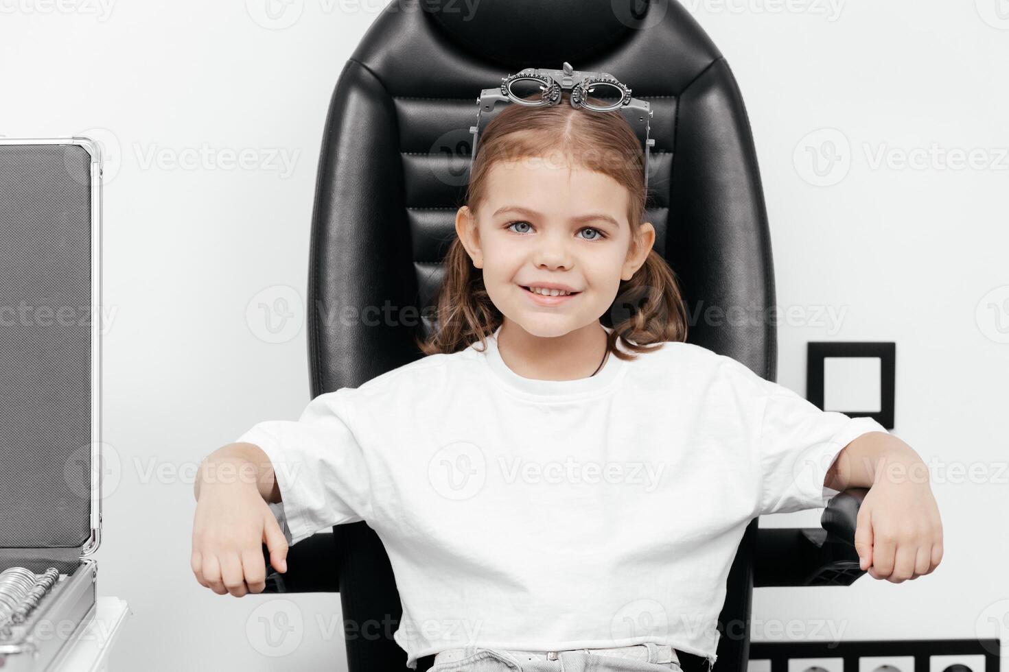 Portrait of a little, happy girl in ophthalmology clinic. Ophthalmic instrument. Excellent moment to illustrate careful examination for children's eye health. Advertisement for pediatric ophthalmology photo