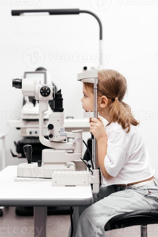 Portrait of a little, happy girl in ophthalmology clinic. Ophthalmic instrument. Excellent moment to illustrate careful examination for children's eye health. Advertisement for pediatric ophthalmology photo