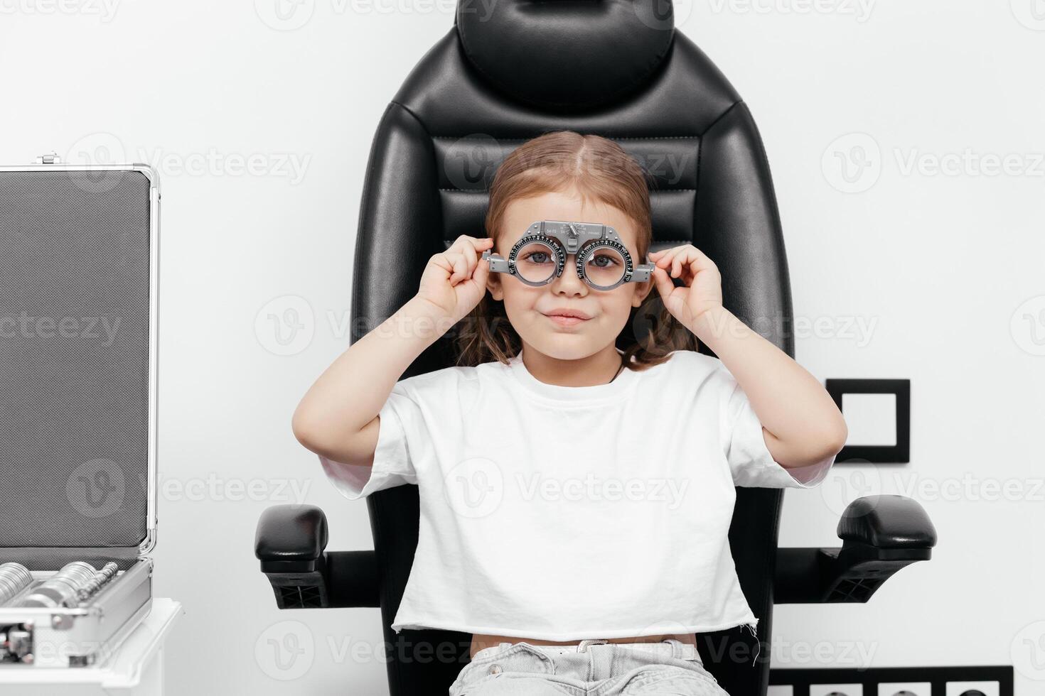 Portrait of a little, happy girl in ophthalmology clinic. Ophthalmic instrument. Excellent moment to illustrate careful examination for children's eye health. Advertisement for pediatric ophthalmology photo