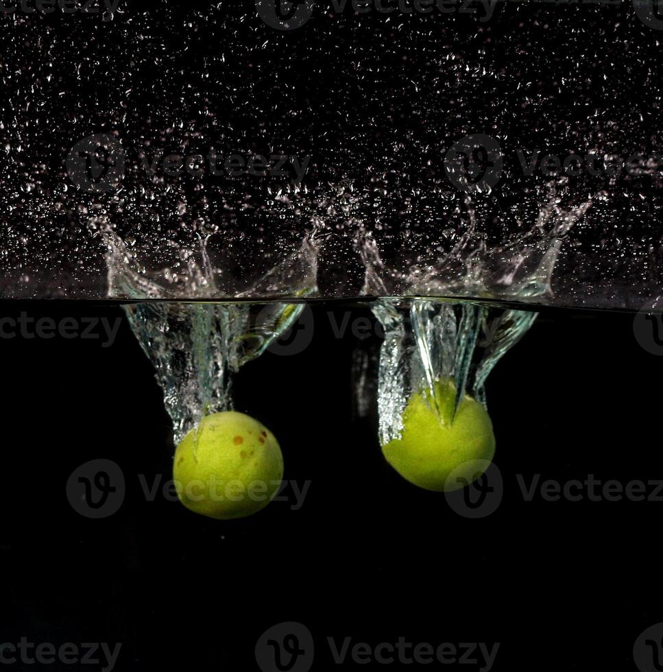 Two apples are falling into water with water splashing on them photo