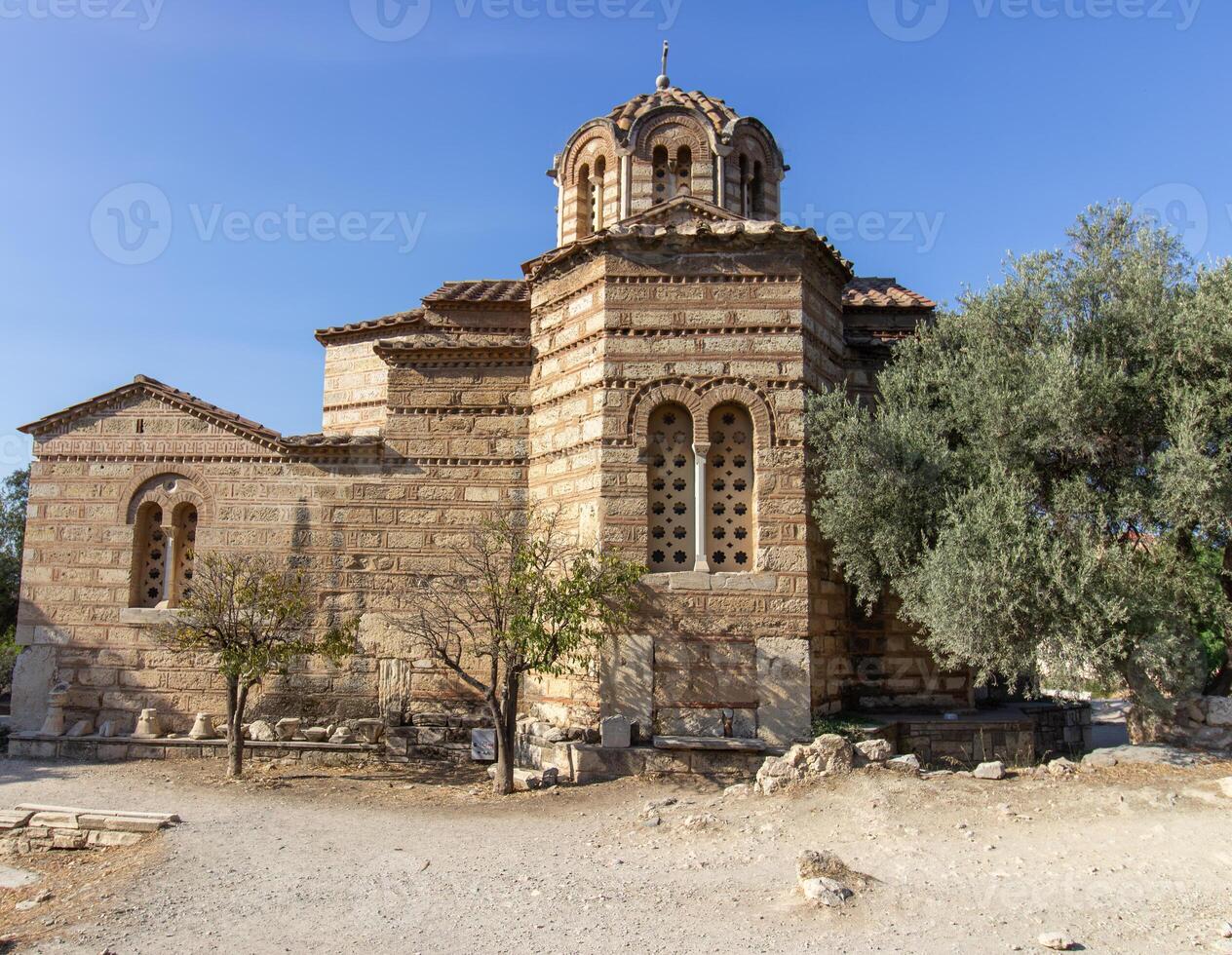 Ancient Byzantine-style stone church with domed roof and cross on top, surrounded by trees and path in Athens, Greece. Outdoor architectural photography photo