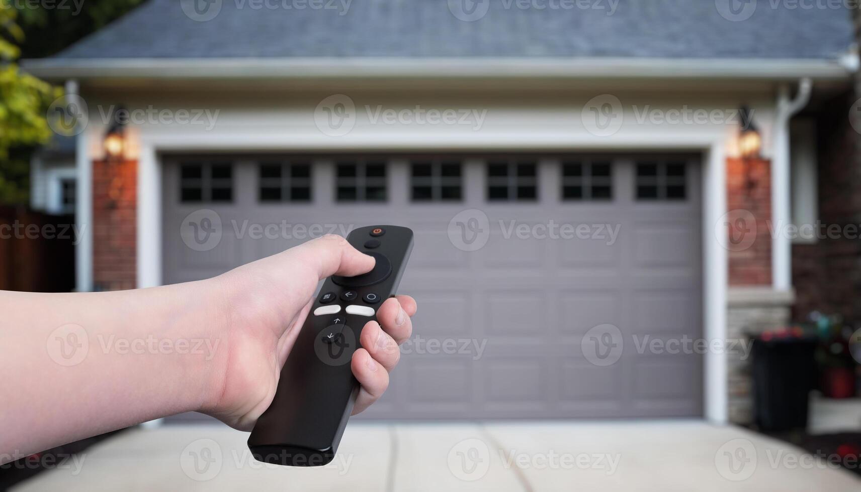 Hand holding a remote control, opening or closing garage doors in a residential setting. Concept of automated home entry, convenience, and modern technology photo