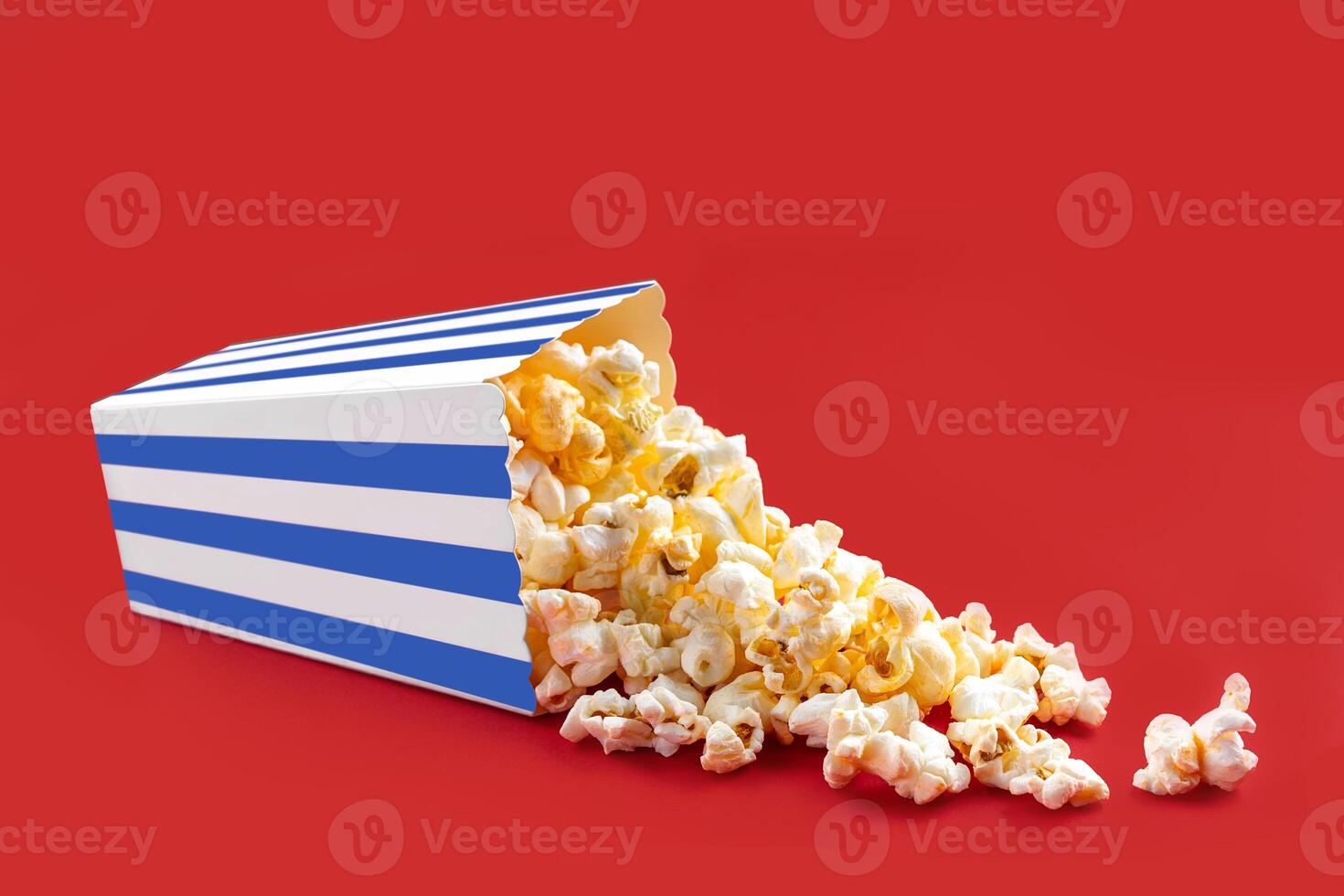 Tasty cheese popcorn falling out of a blue striped carton bucket, isolated on red background photo