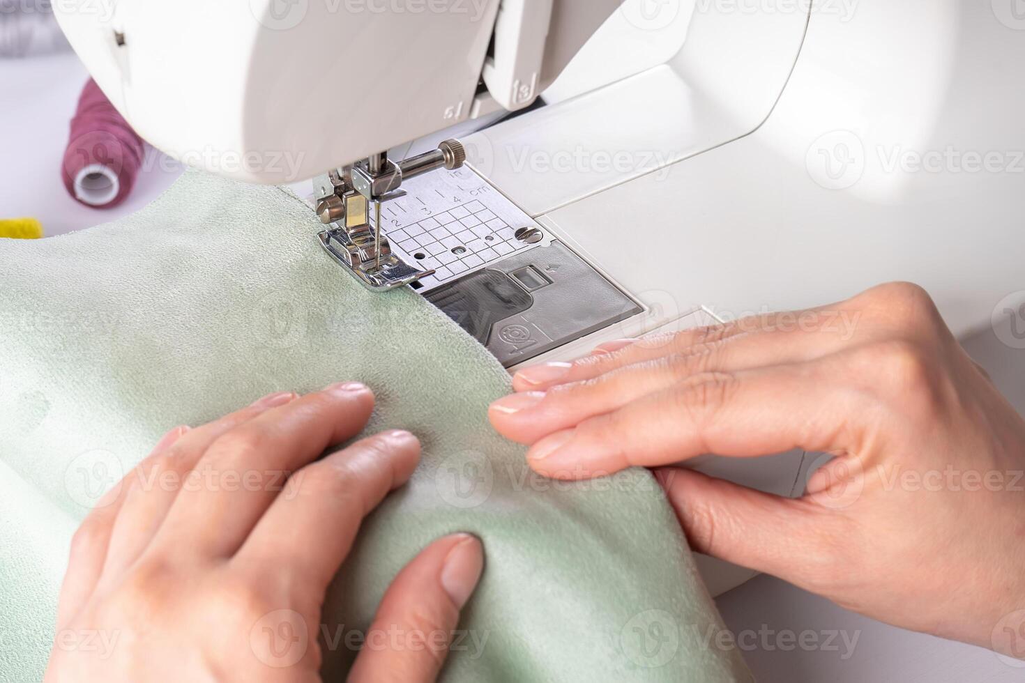 Female hands stitching green fabric on modern sewing machine at workplace in atelier photo