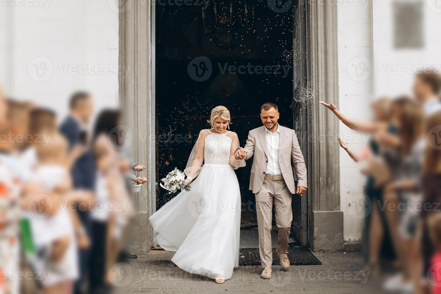 Smiling and happy young married couple leaving church after marriage. Launch of confetti, confetti and flower petals that are good wishes for marriage. photo