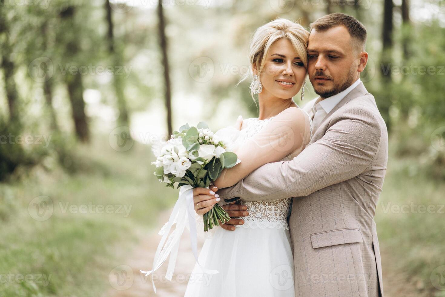 Wedding couple bride and groom hugging in pine forest, sunlight filtering through the trees, highlighting their joyful expressions. photo