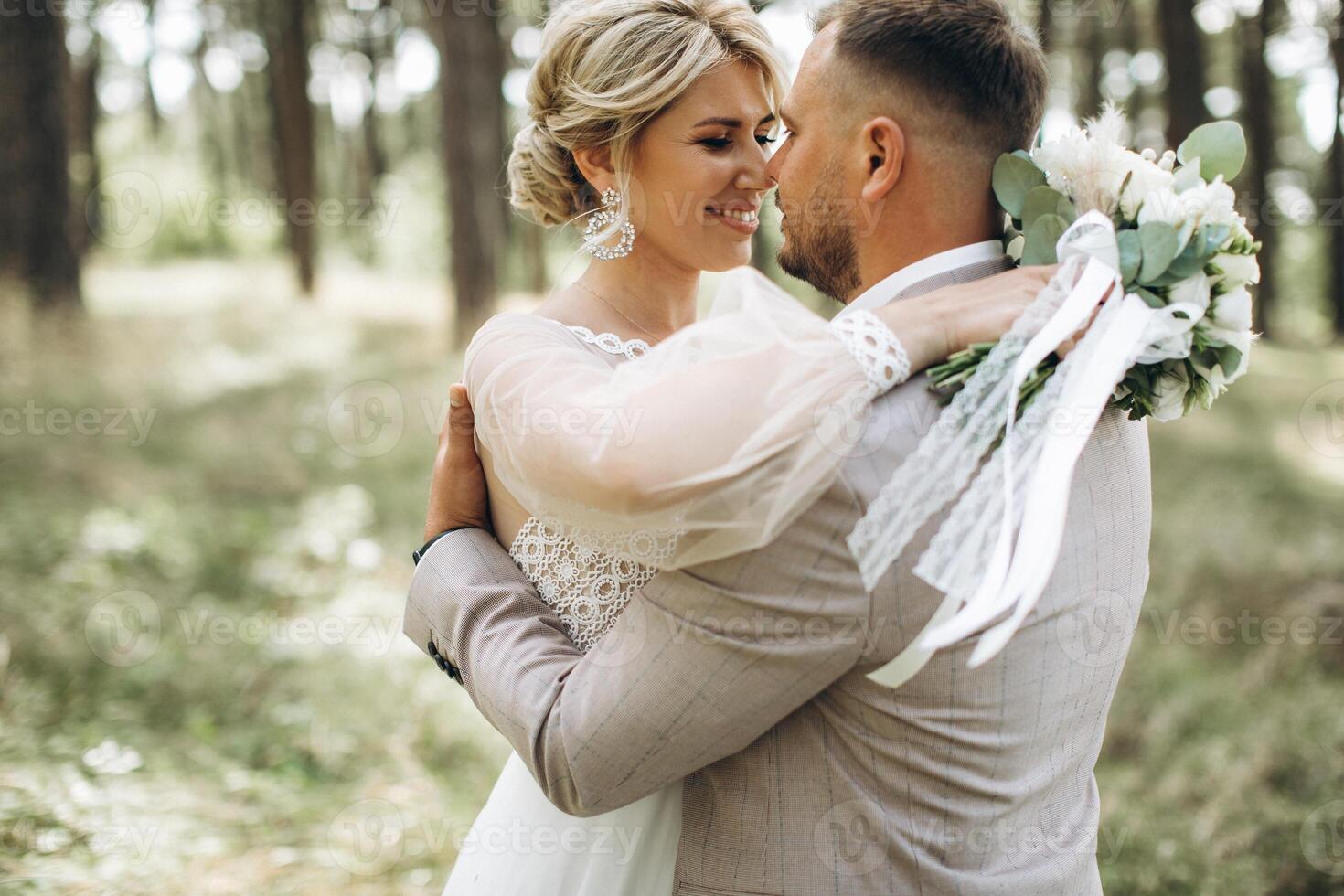 Wedding couple bride and groom hugging in pine forest, sunlight filtering through the trees, highlighting their joyful expressions. photo