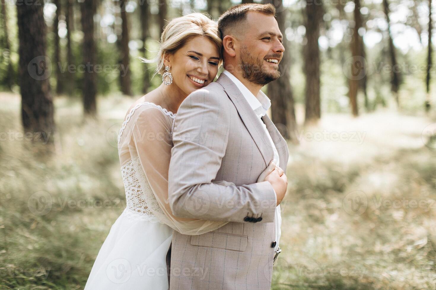 Wedding couple bride and groom walk hand in hand through a pine forest, sunlight filtering through the trees, highlighting their joyful expressions. photo