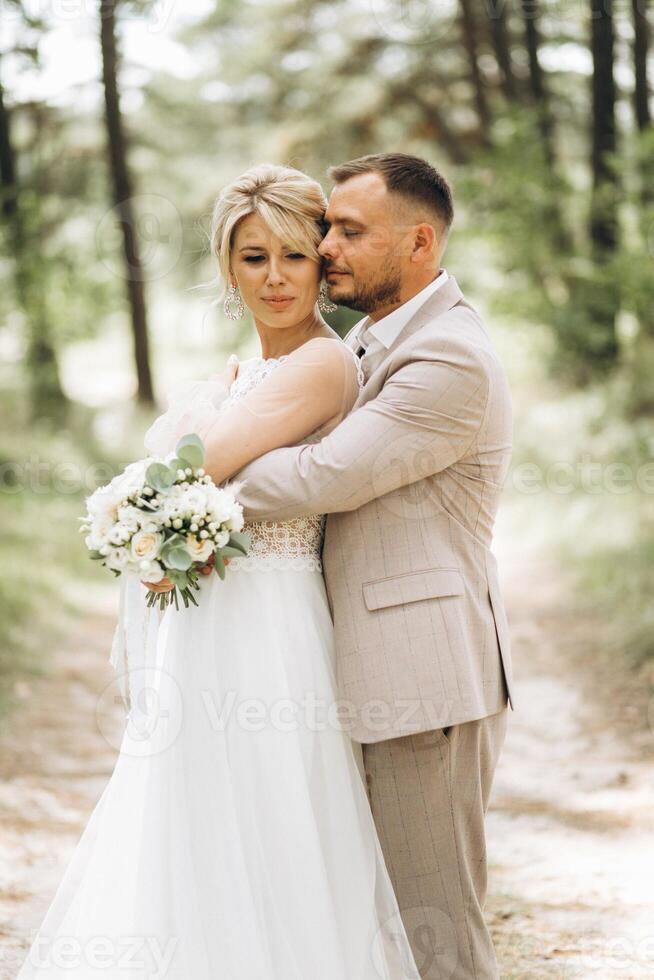 Wedding couple bride and groom hugging in pine forest, sunlight filtering through the trees, highlighting their joyful expressions. photo