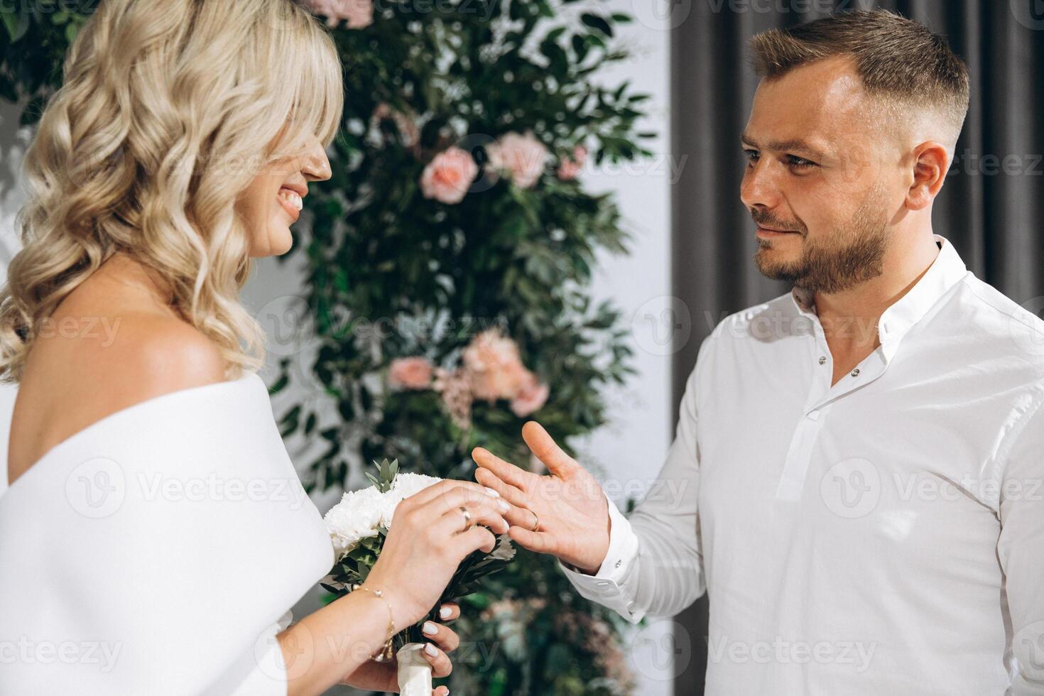 Joyful Wedding Couple Exchanging Rings in a Beautiful Ceremony with Floral Background Decorations photo
