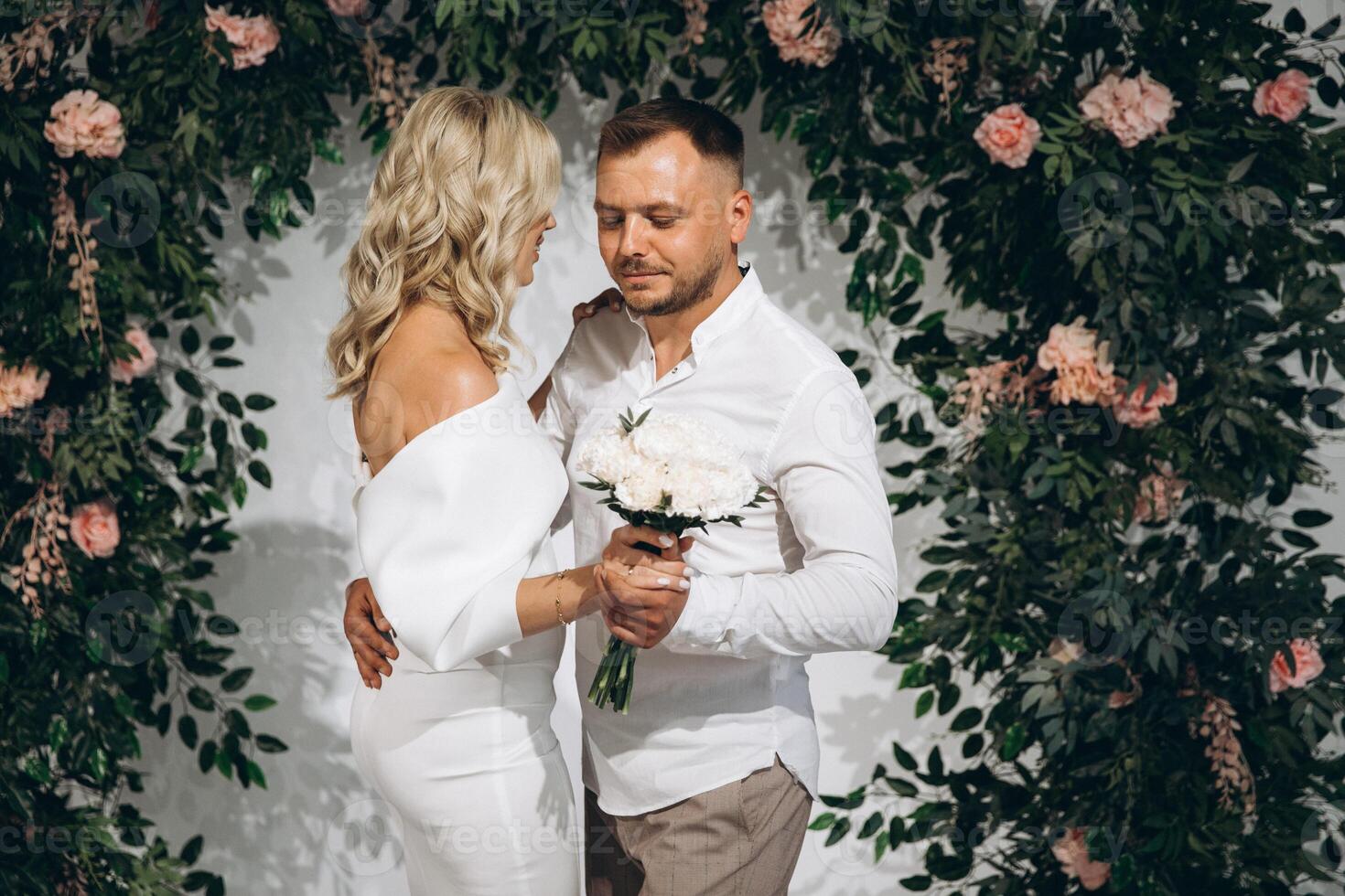 Romantic Wedding Portrait of a Couple Embracing in Front of Lush Greenery and Floral Backdrop photo
