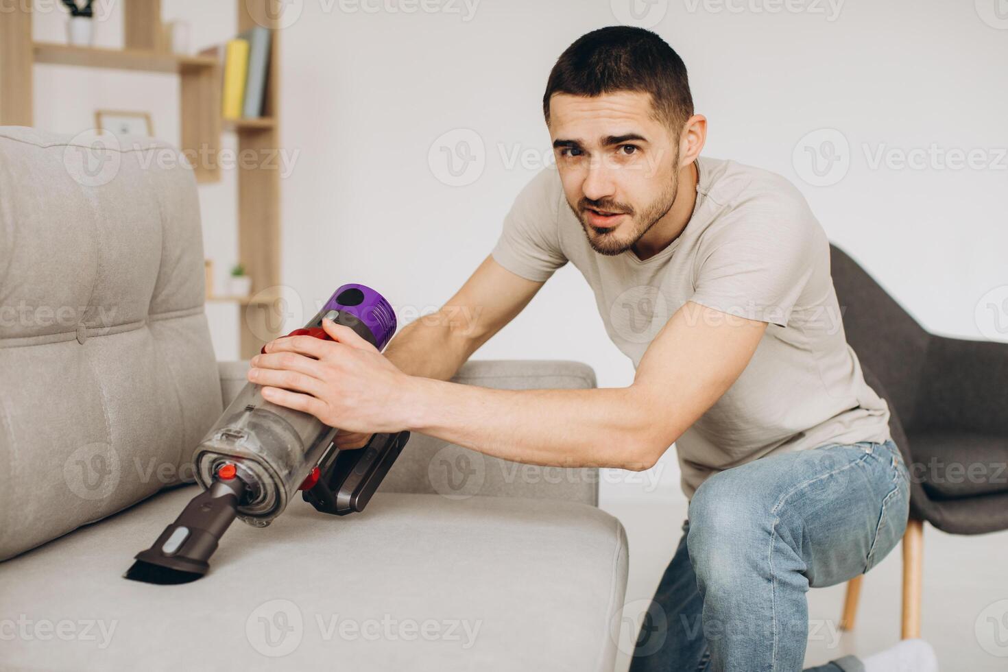 A young man cleans the sofa with a vacuum cleaner photo