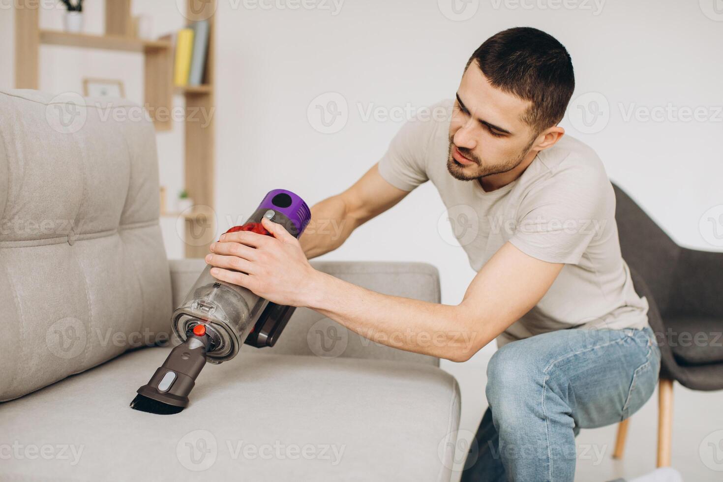 A young man cleans the sofa with a vacuum cleaner photo