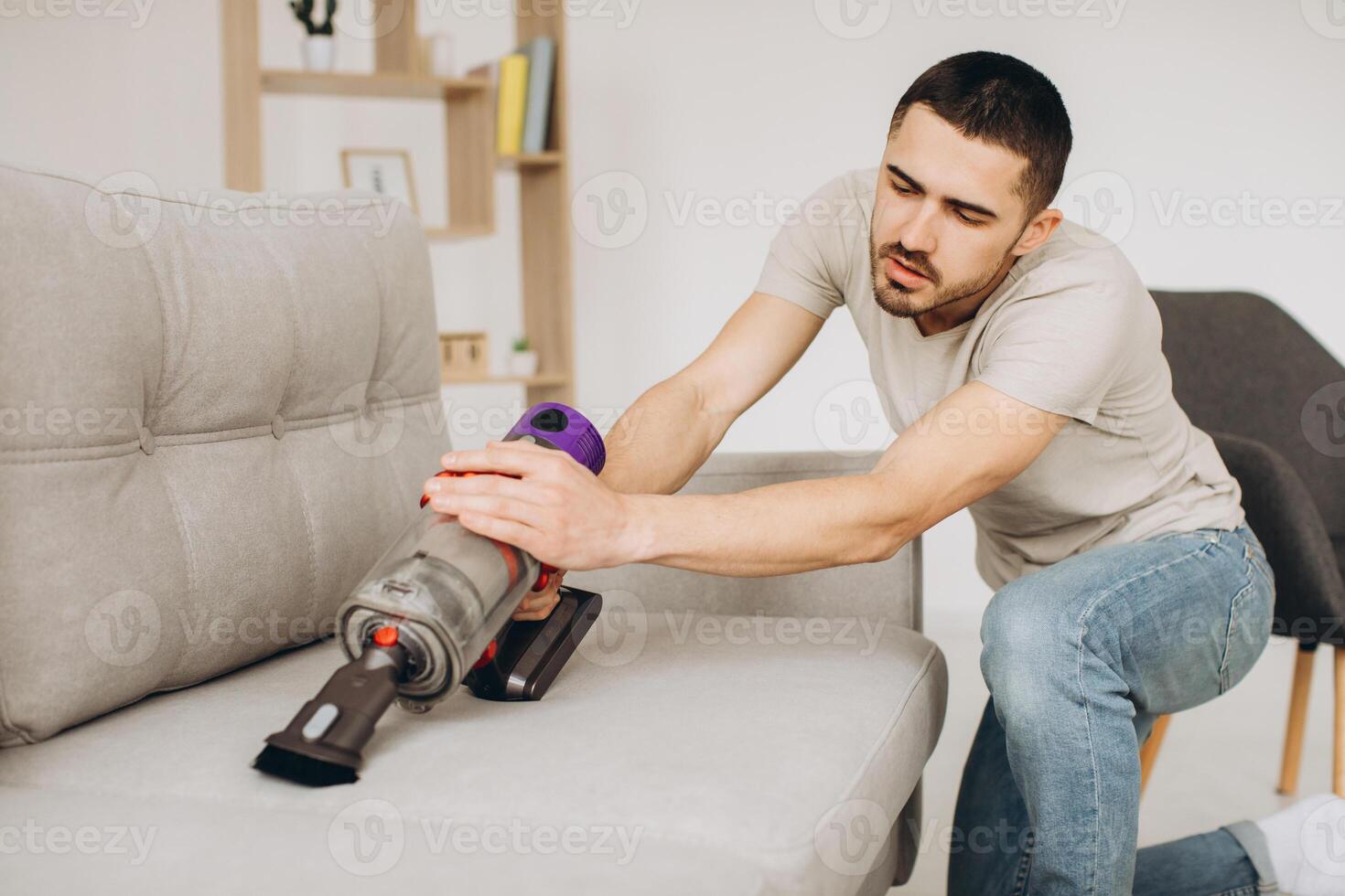 A young man cleans the sofa with a vacuum cleaner photo