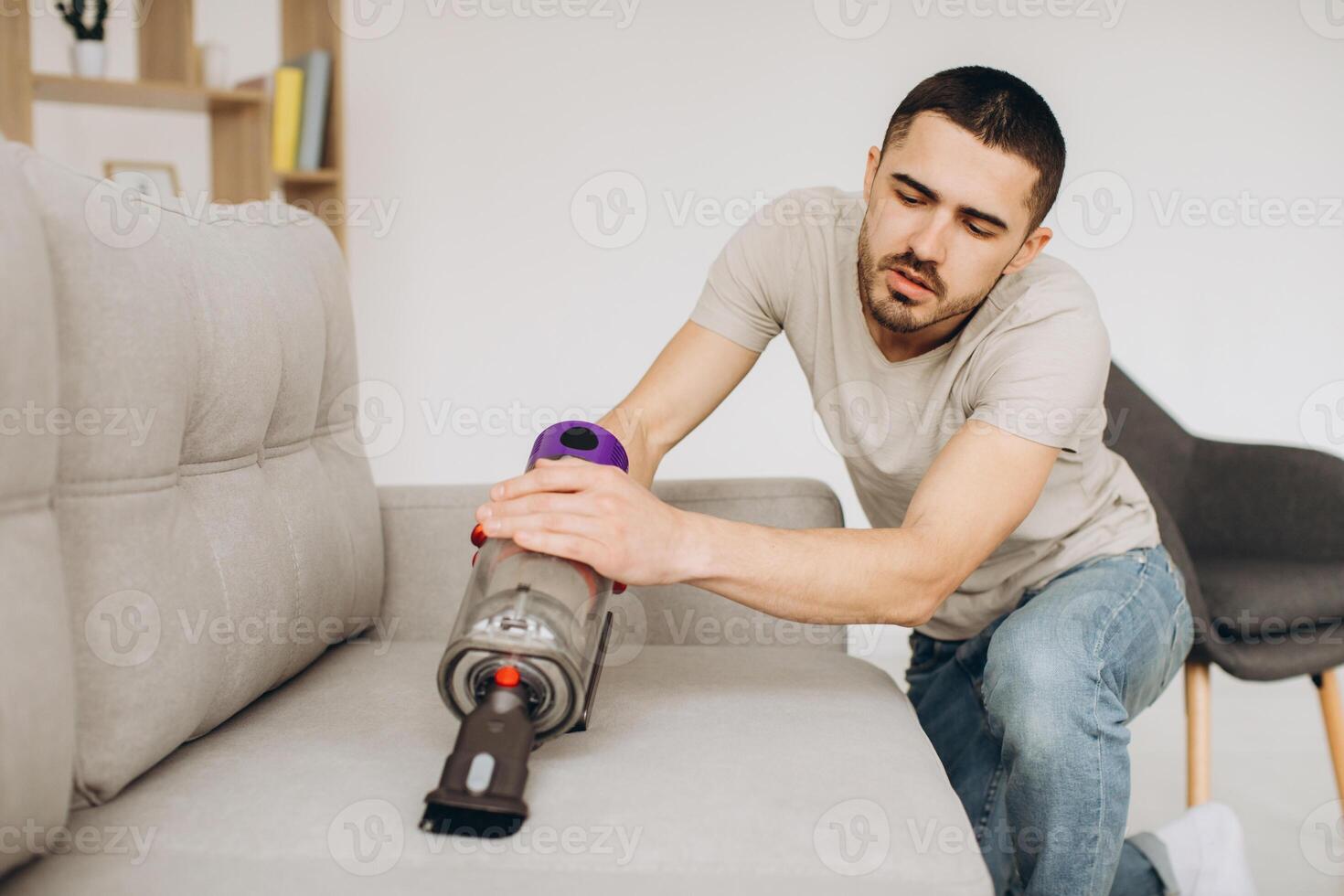 A young man cleans the sofa with a vacuum cleaner photo