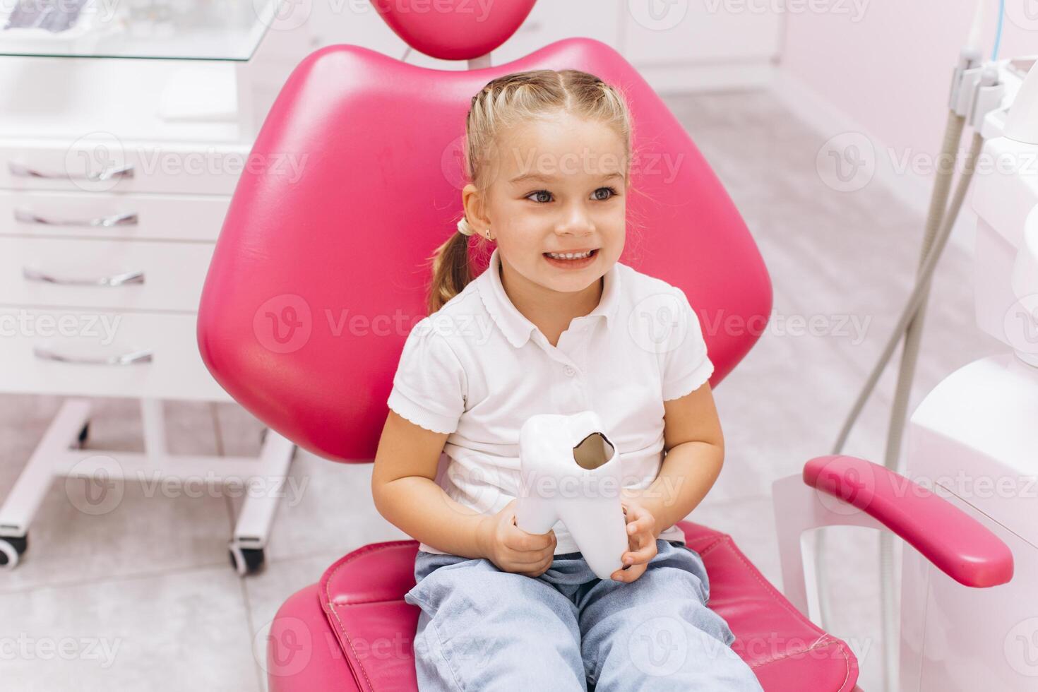 Little girl smiling on a visit to the dentist holding a tooth model at the dental clinic photo