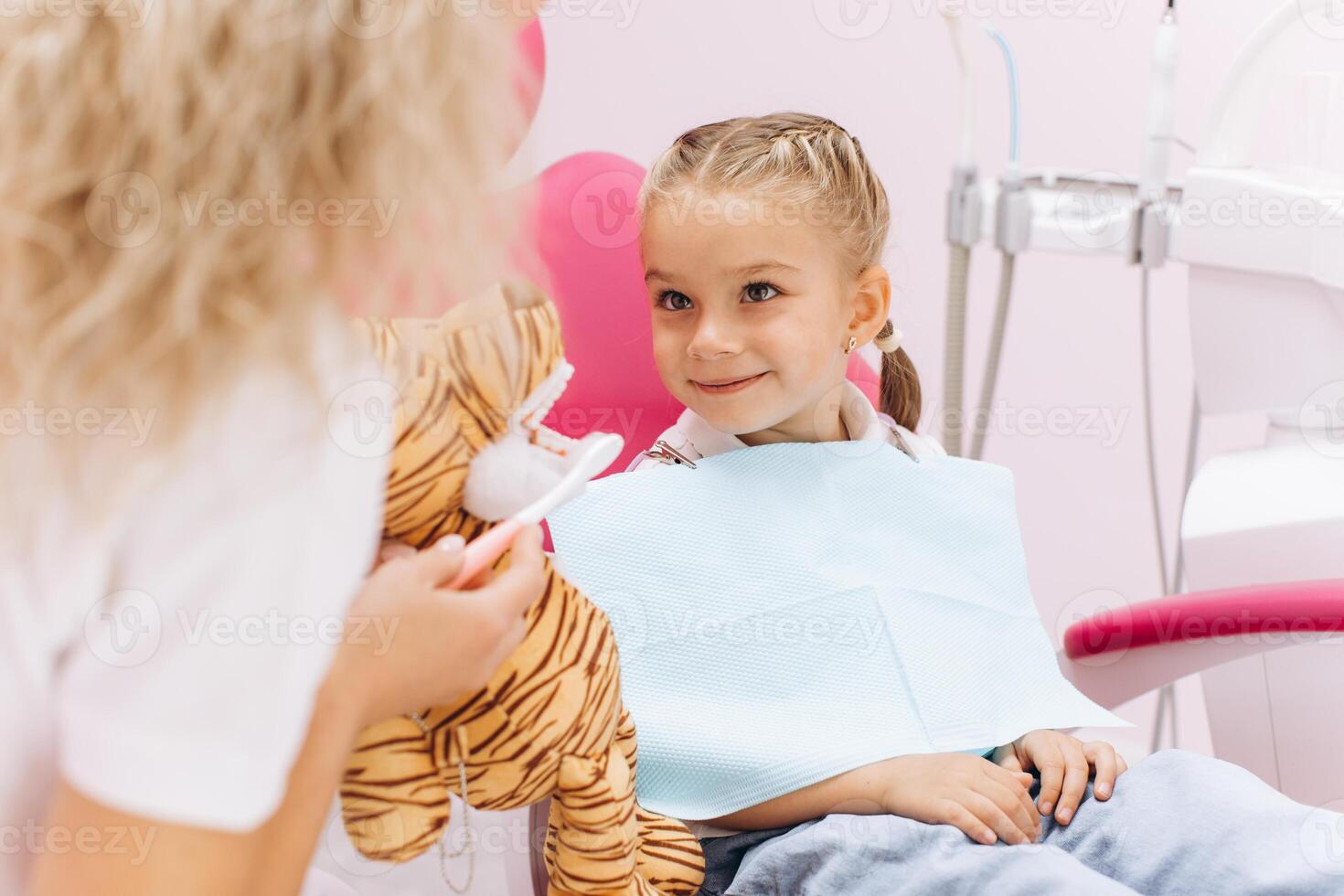 Little girl on a visit to the dentist holding a toy and showing how to brush your teeth in a dental clinic photo