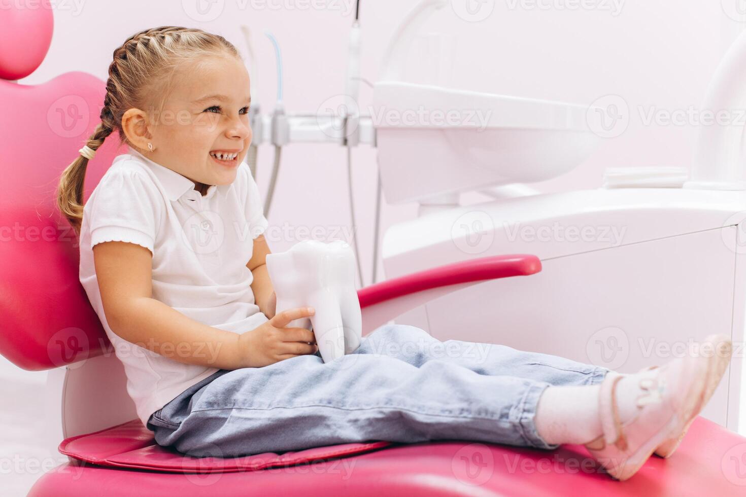 Little girl smiling on a visit to the dentist holding a tooth model at the dental clinic photo