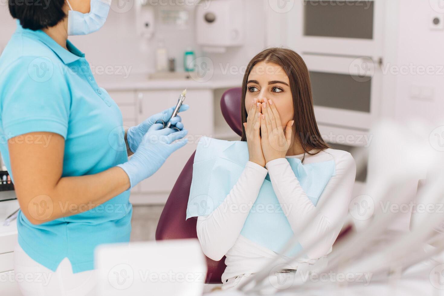 The dentist injects anesthesia to the girl patient, she is scared. photo
