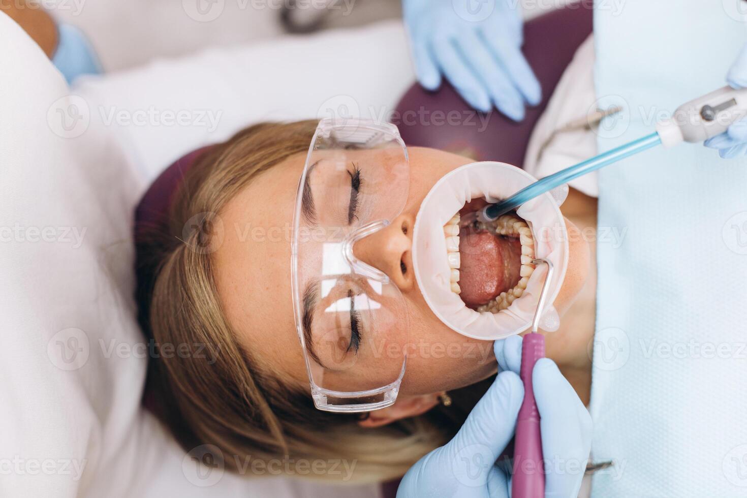 Face of a woman in goggles and a dilator in her mouth during dental treatment with dental instruments at the clinic photo