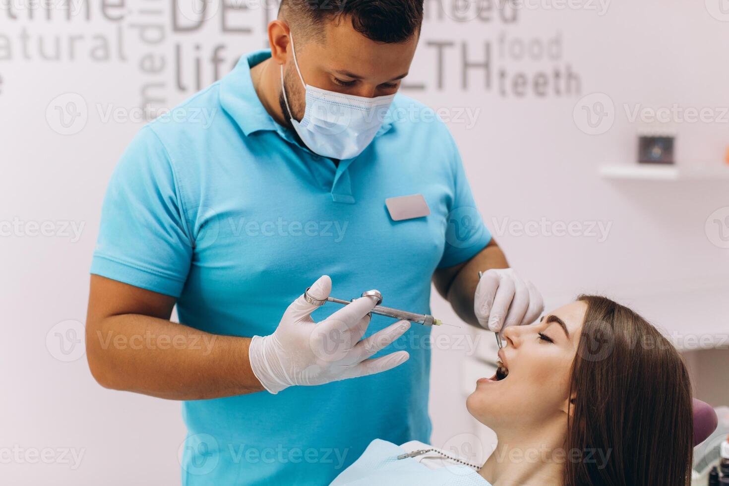 The dentist injects anesthesia to the girl patient, she is scared. photo