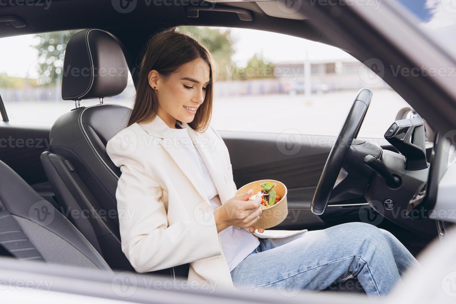 Young Woman Eating Healthy Salad Lunch in Car While Taking a Break From Work, Dressed in Casual Blazer and Jeans on a Relaxing Day photo