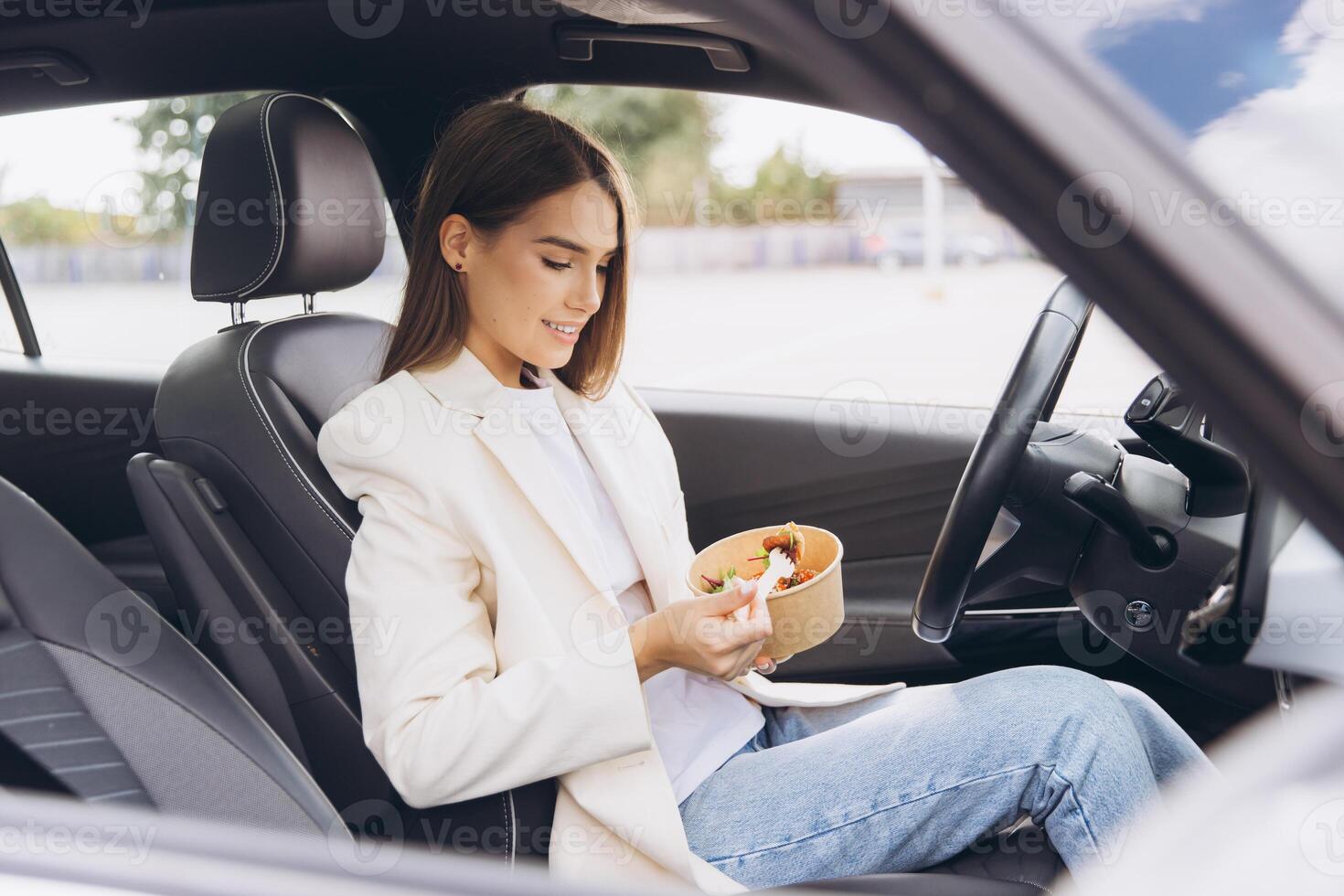 Young Woman Eating Healthy Salad Lunch in Car While Taking a Break From Work, Dressed in Casual Blazer and Jeans on a Relaxing Day photo
