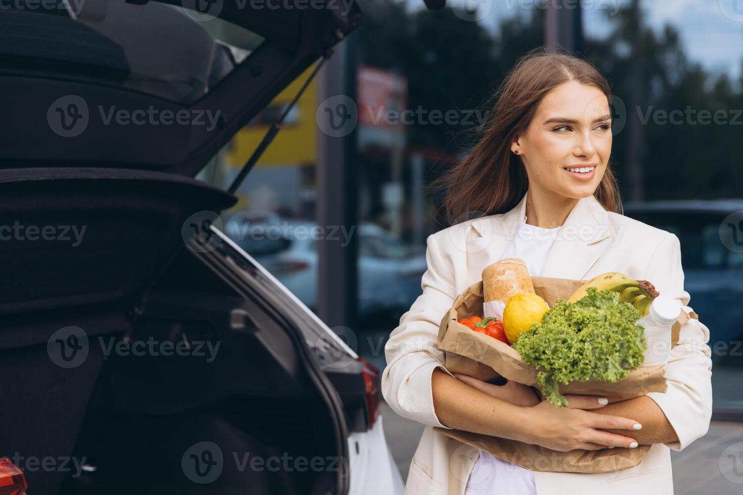 Young Woman Loading Groceries Into Car Trunk at Supermarket photo