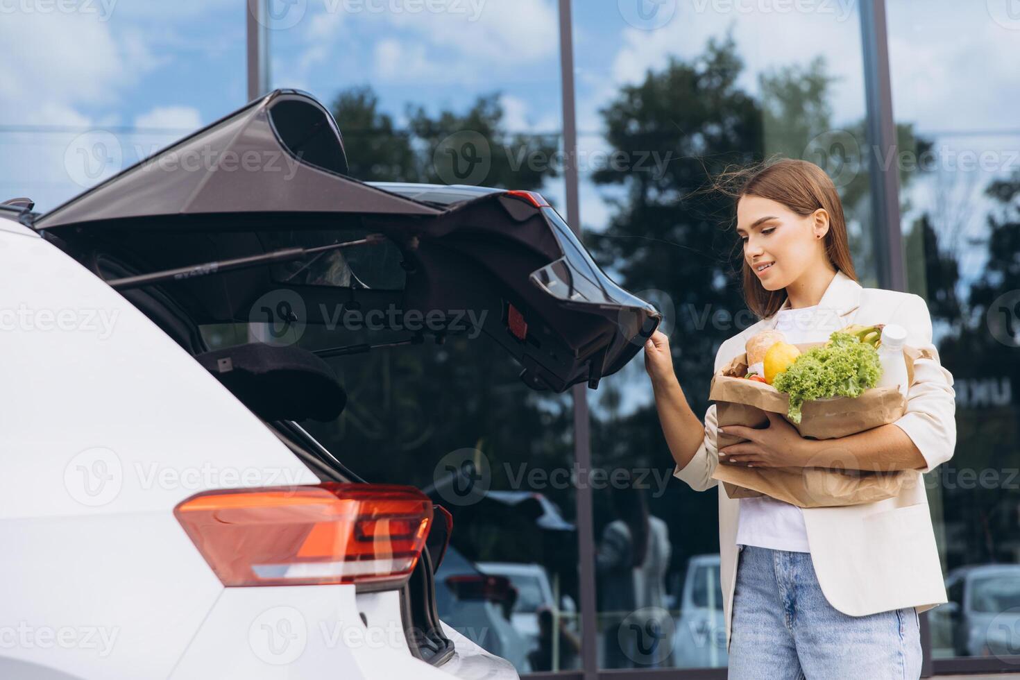 Young Woman Loading Groceries Into Car Trunk After Shopping photo