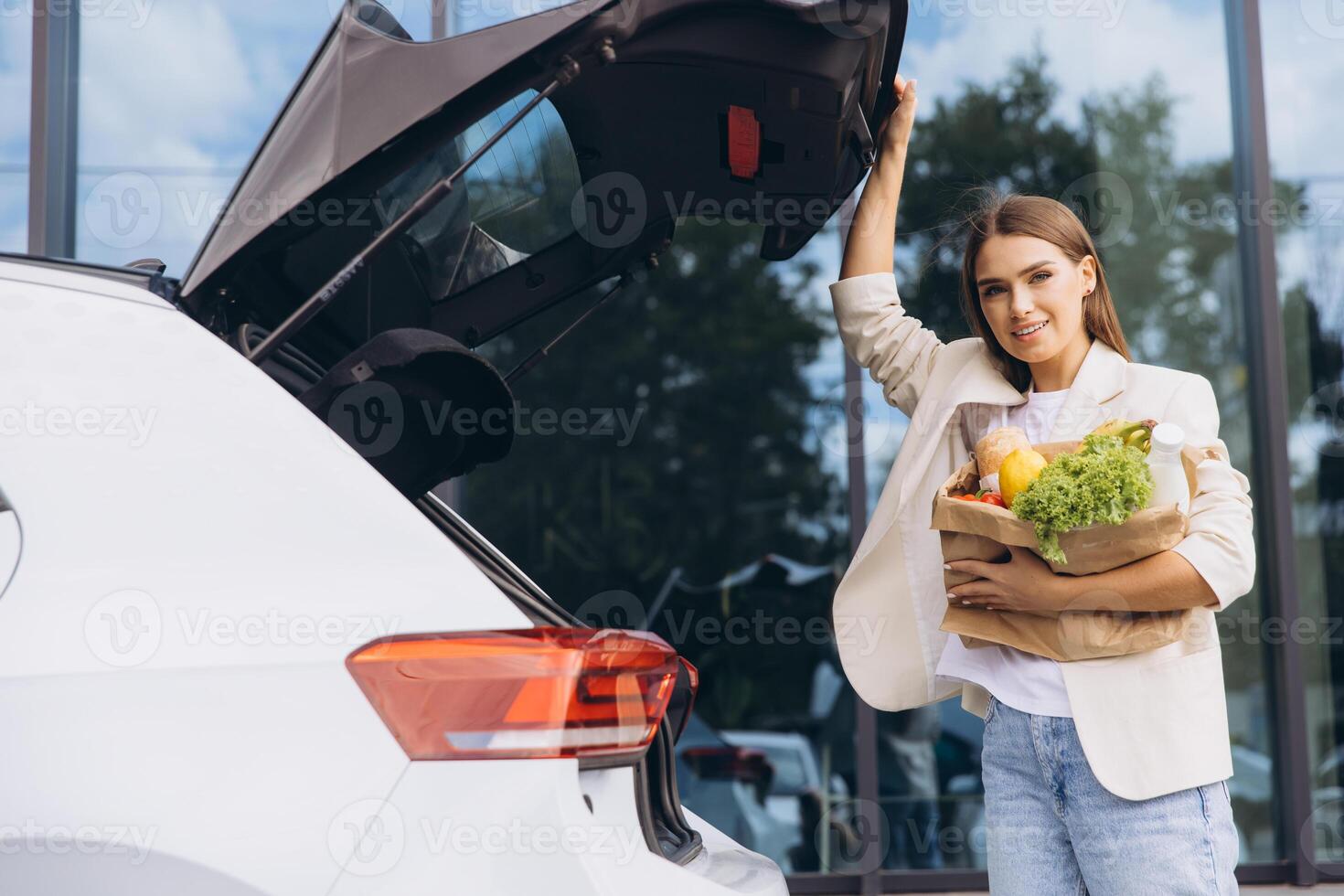Young Woman Loading Groceries Into Car Trunk Outdoors photo